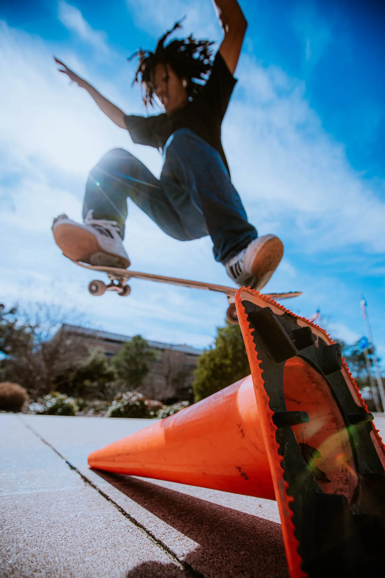 Skateboarder jumping over a traffic cone on a sunny day.