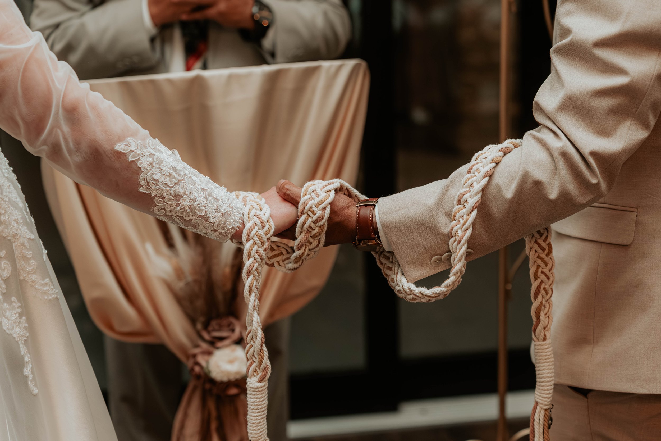 A bride and groom holding hands during a wedding ceremony, with a thick rope symbolizing their vows.