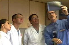 Four medical professionals, three men and one woman, taking a selfie in a hospital or clinical setting.