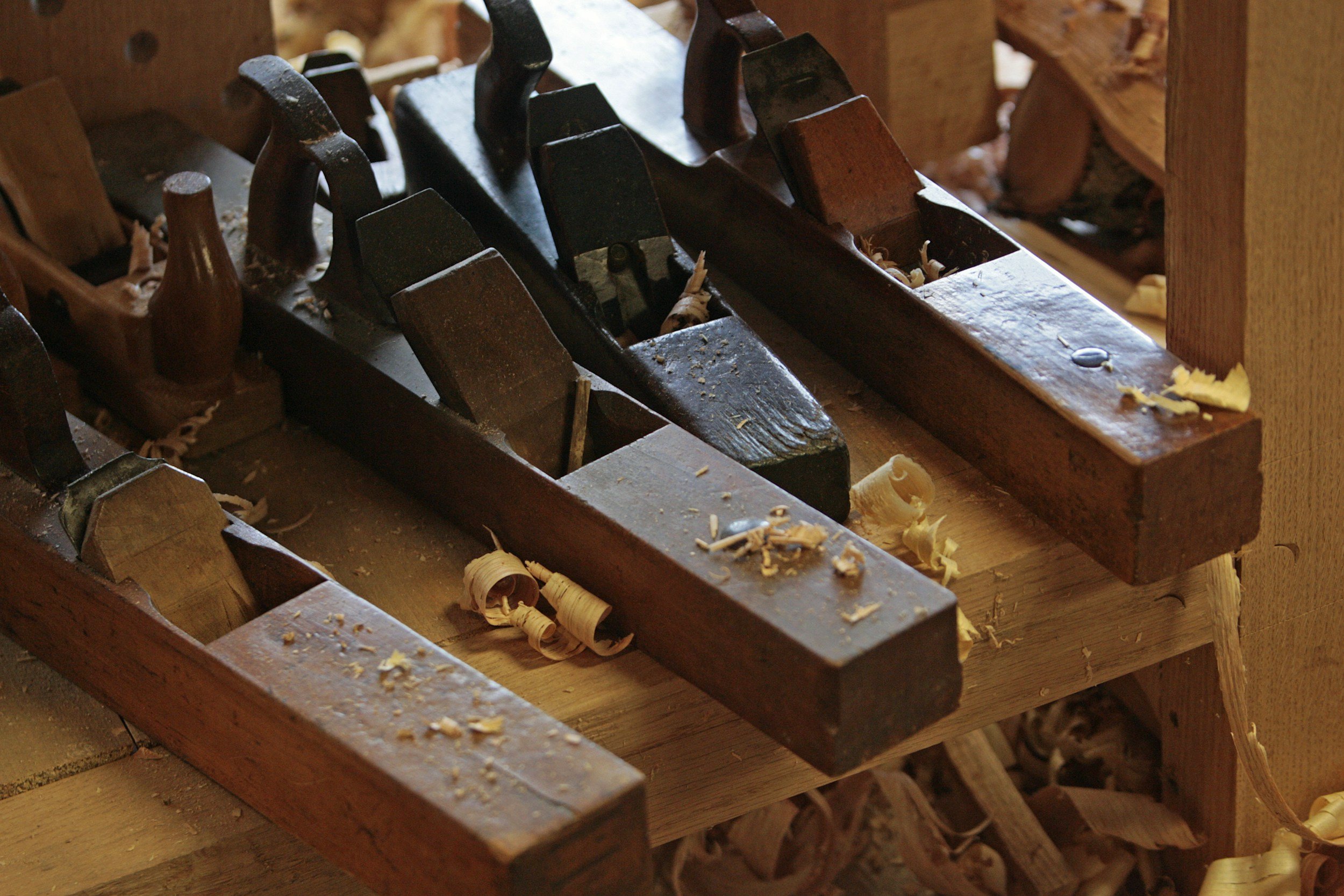 Close-up of vintage woodworking planes on a wooden workbench with wood shavings around.
