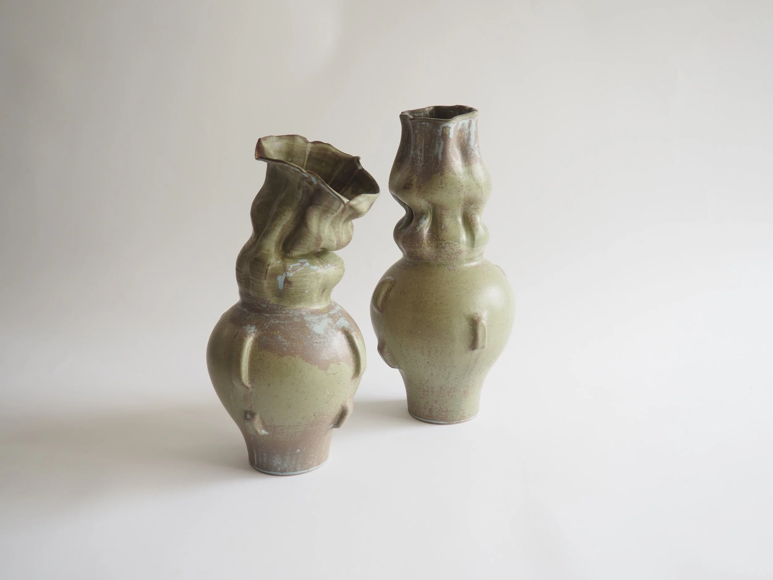 Two ceramic vases with abstract, wavy designs and a muted green and beige glaze, set against a plain white background.