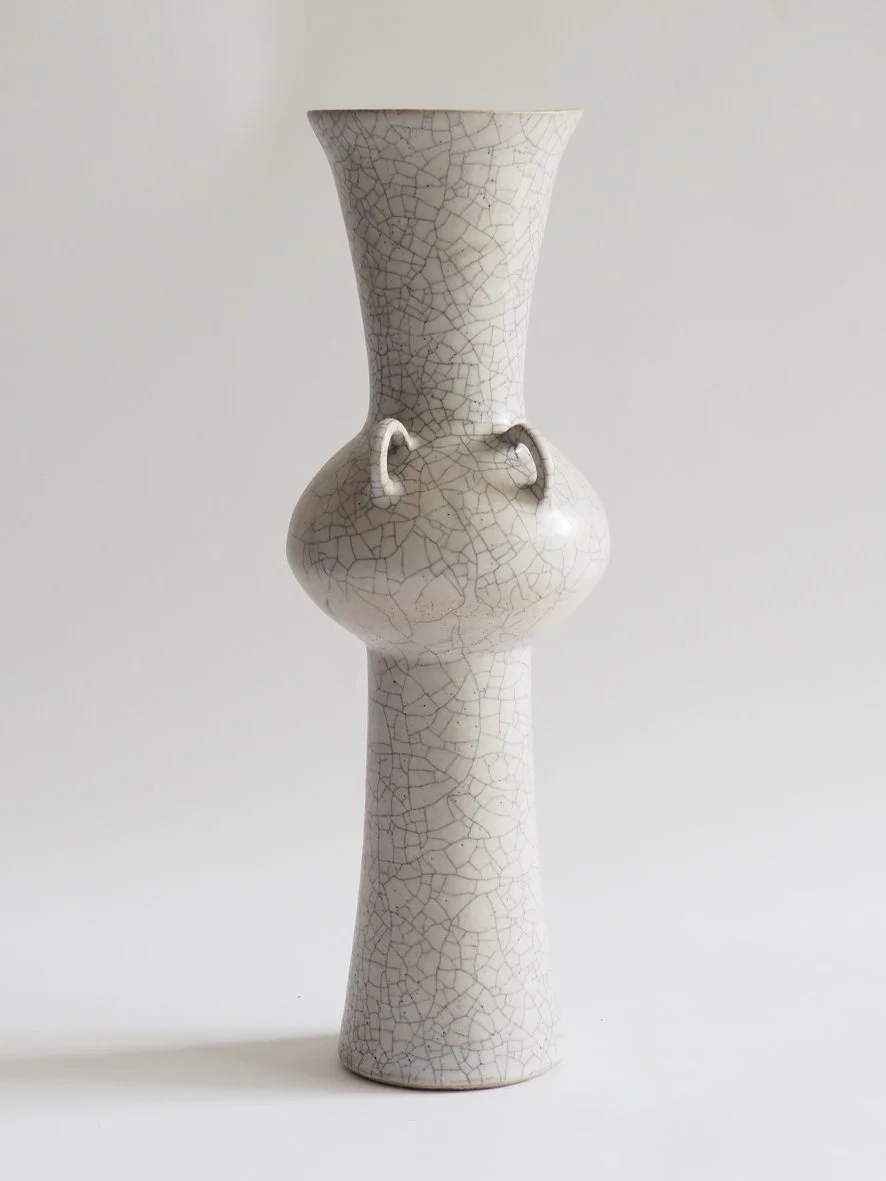 A tall ceramic vase with a crackle glaze finish, featuring a bulbous middle section with small handles and a wide top opening.
