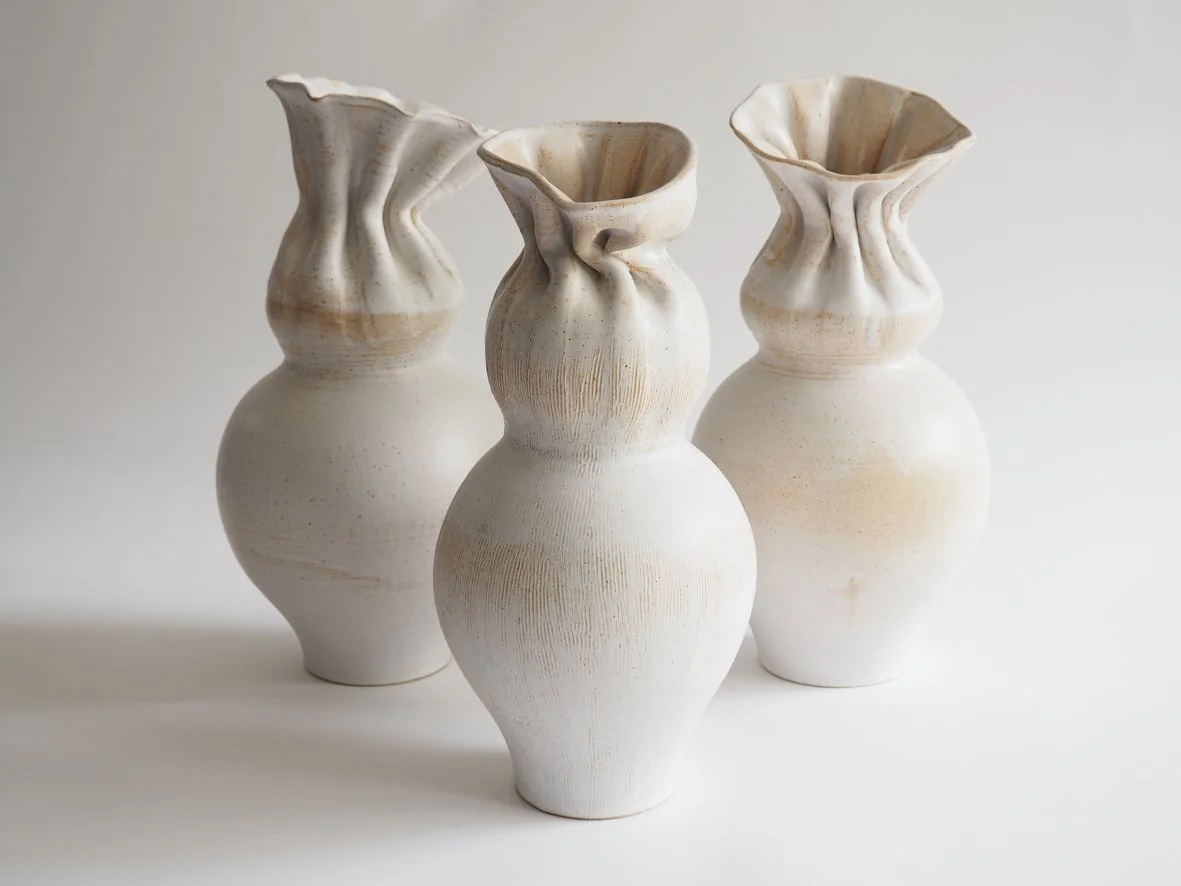 Three off-white ceramic vases with textured surfaces and wavy, ruffled openings, arranged on a white surface against a light background.