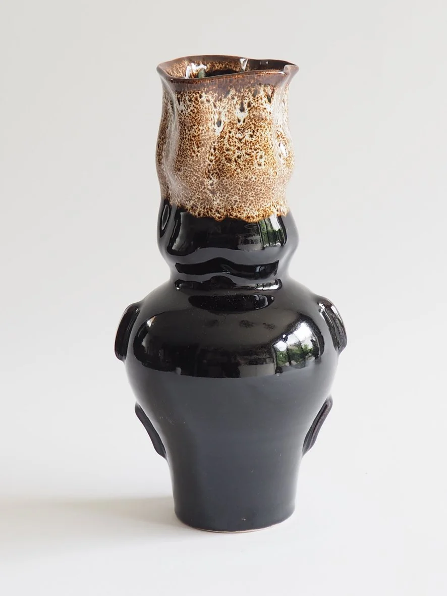 A unique ceramic vase with a glossy black base and a textured, brown and speckled top.