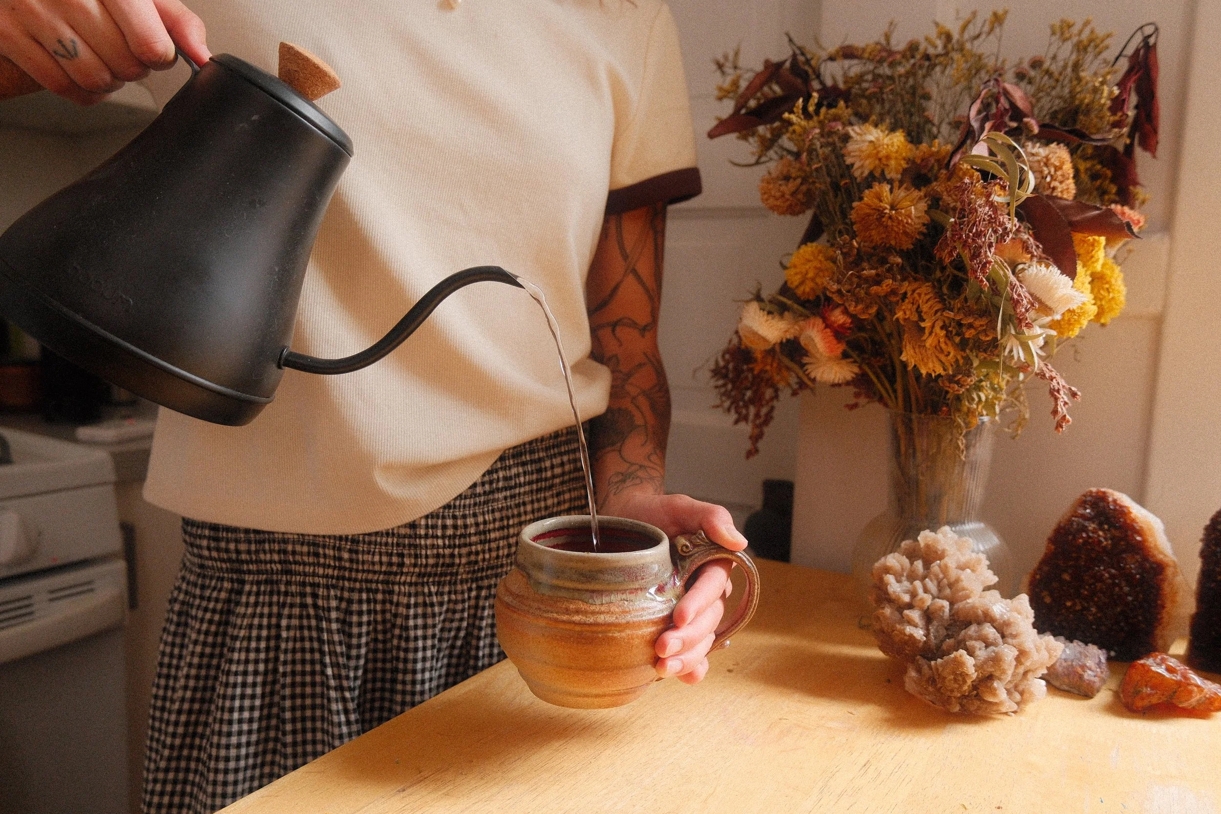 Sam Cuneo, Denver based birth and postpartum doula, pours tea from a black teapot into a ceramic mug.