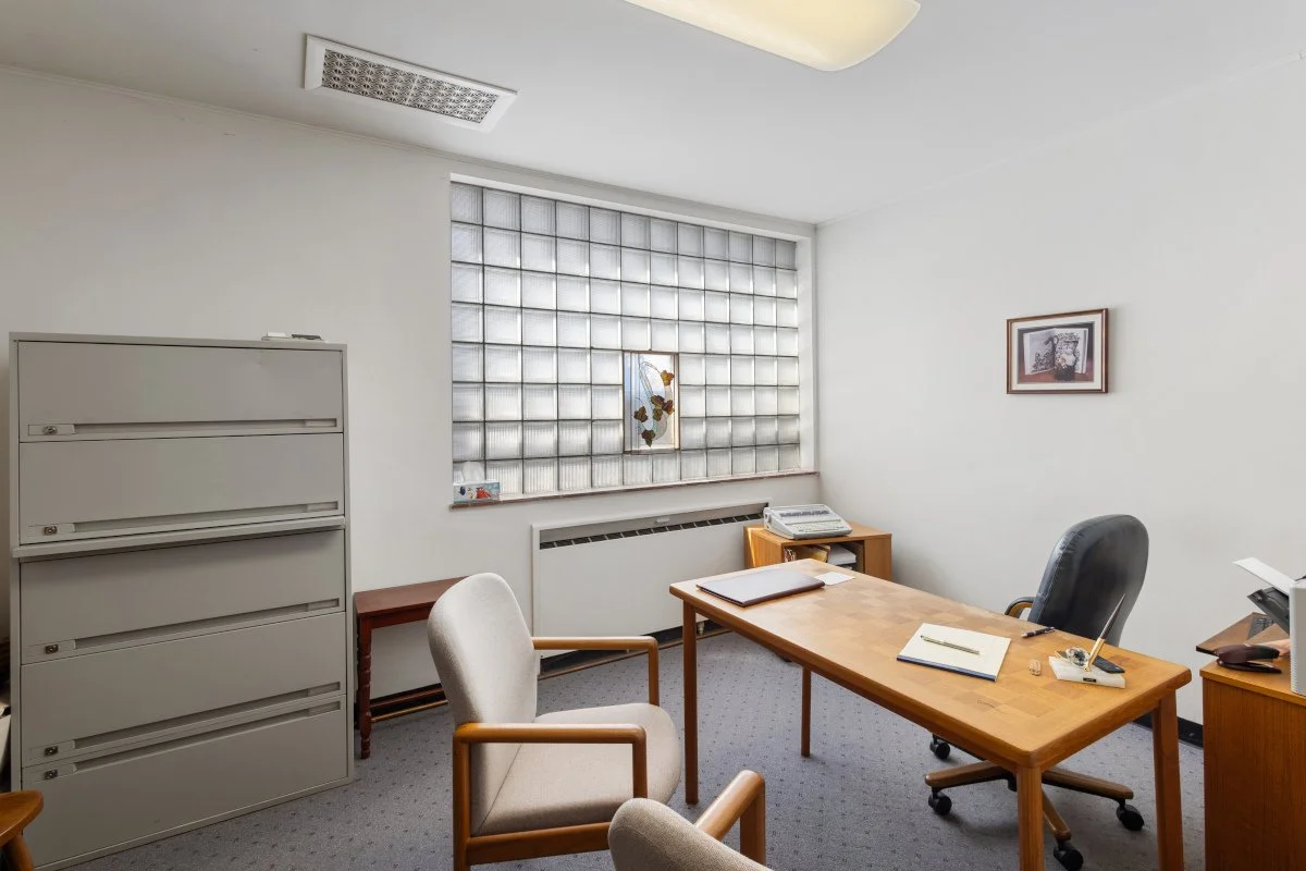 Empty office with wooden desk, gray chair, black office chair, file cabinet, and glass block window.
