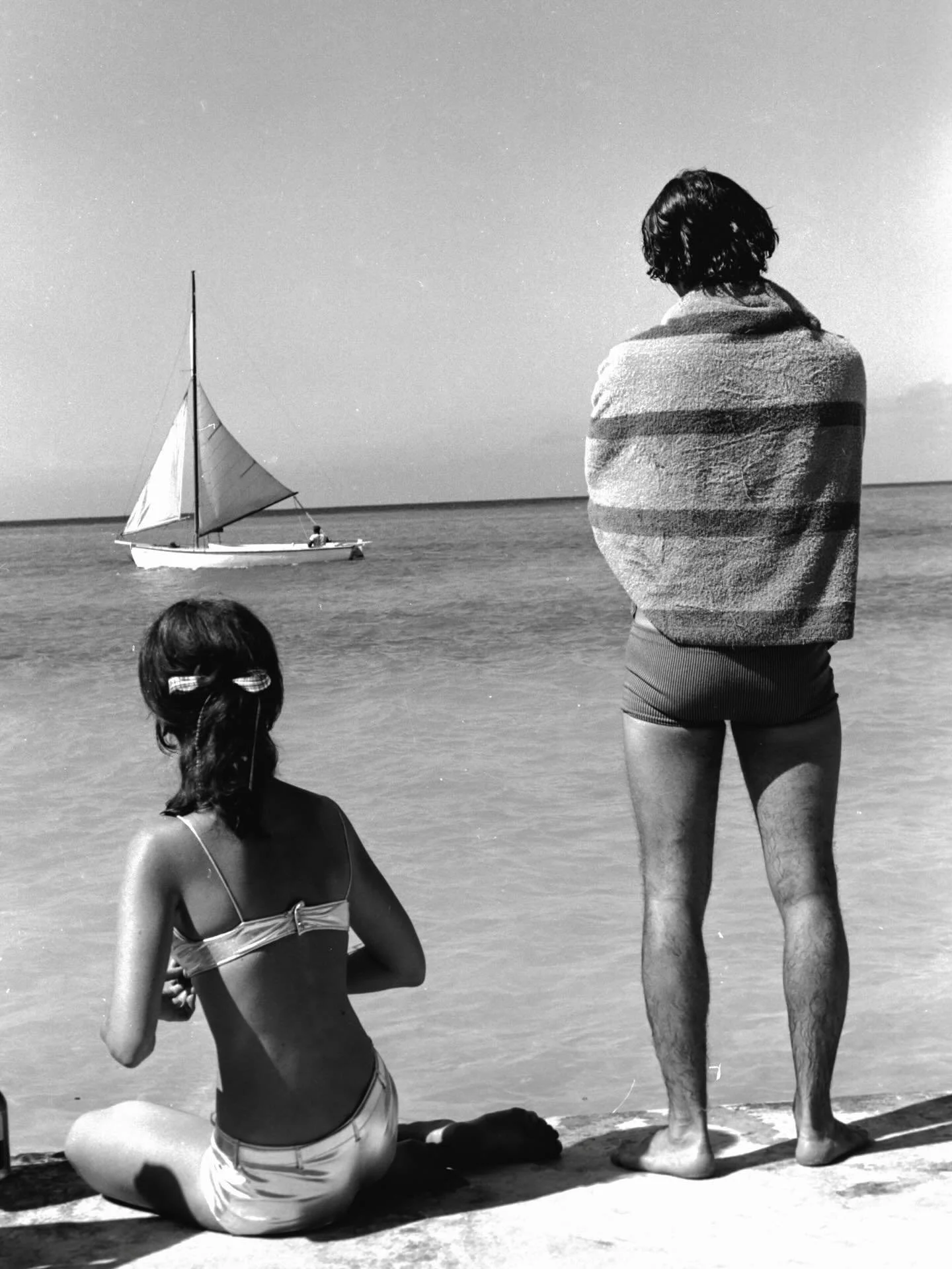 Jamaica, late 1960s

During extended stays in Jamaica, Woodward photographed daily life along the coast&mdash;favoring unposed moments shaped by light, rhythm, and routine. Here, two figures pause at the shoreline as a sailboat passes just offshore.
