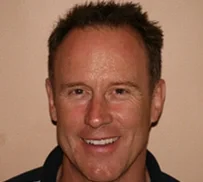 A smiling man with short, reddish-brown hair