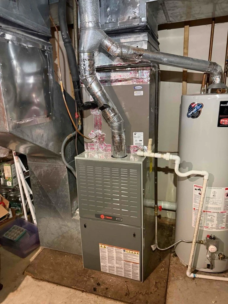 An HVAC furnace with ductwork and a water heater in a basement utility room.