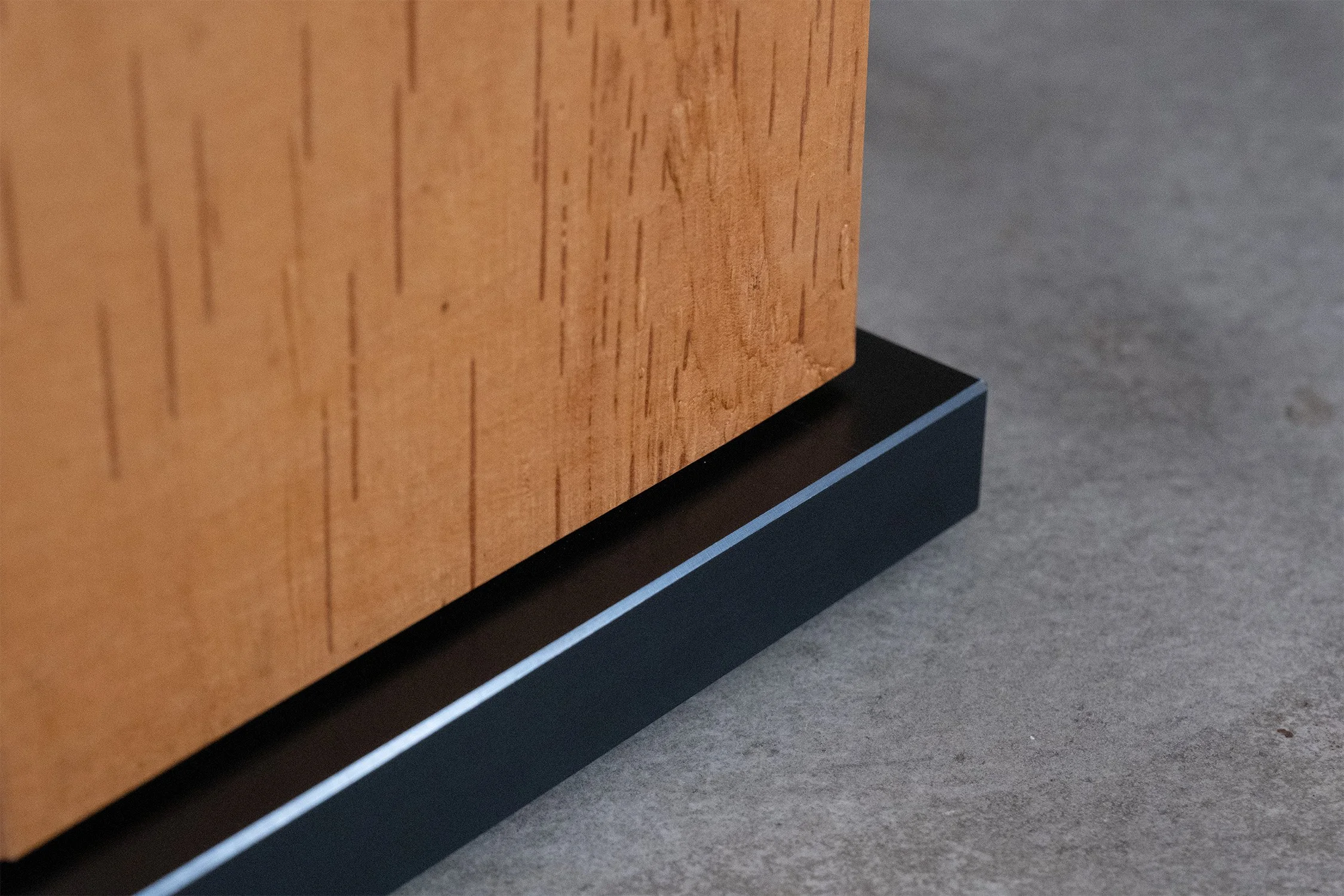 Close-up of the birch bark column meeting the table’s milled, blackened steel base.