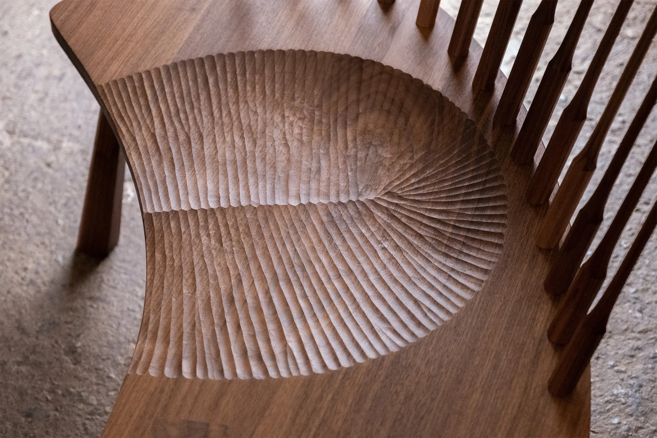 Detail of the curved walnut settee’s carved seat and spindles