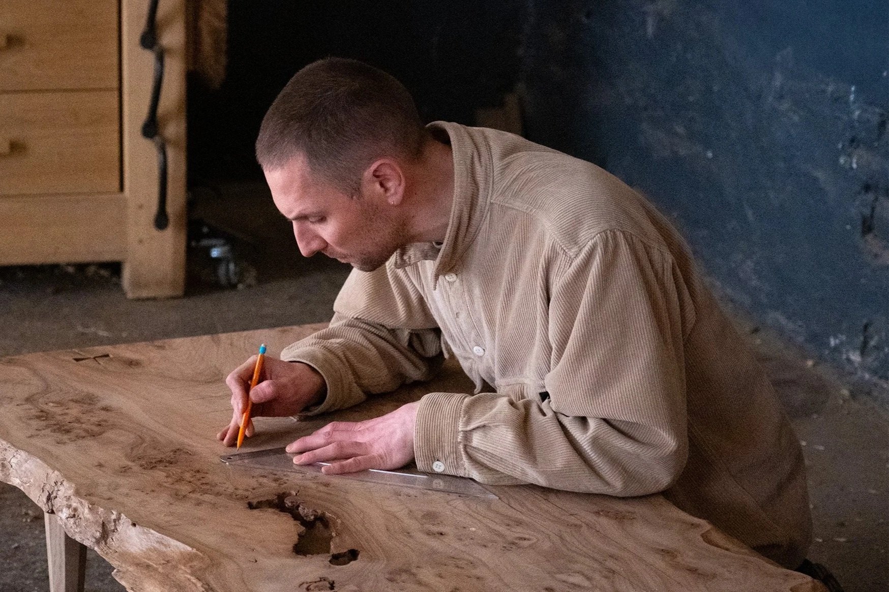 Furniture maker Matthew Hensby marking out a timber slab with a pencil in the workshop.