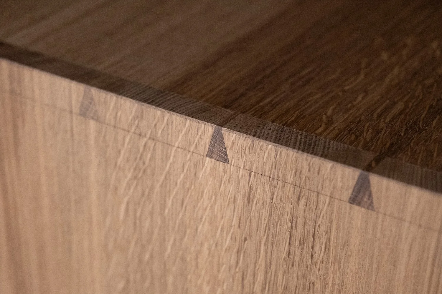 Fine dovetail joints connecting the oak top and side of the bedside cabinet, with visible natural grain.