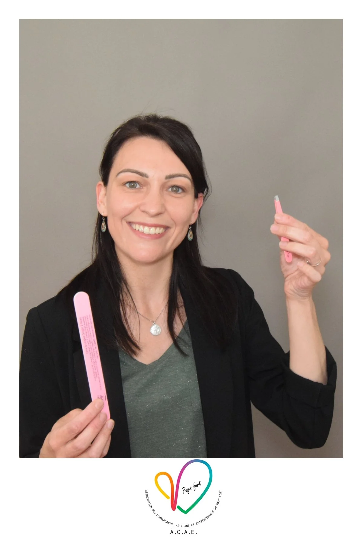 Une femme souriante tenant deux rasoirs roses devant un mur gris, portant un collier et des boucles d'oreilles, avec un badge ou logo en bas