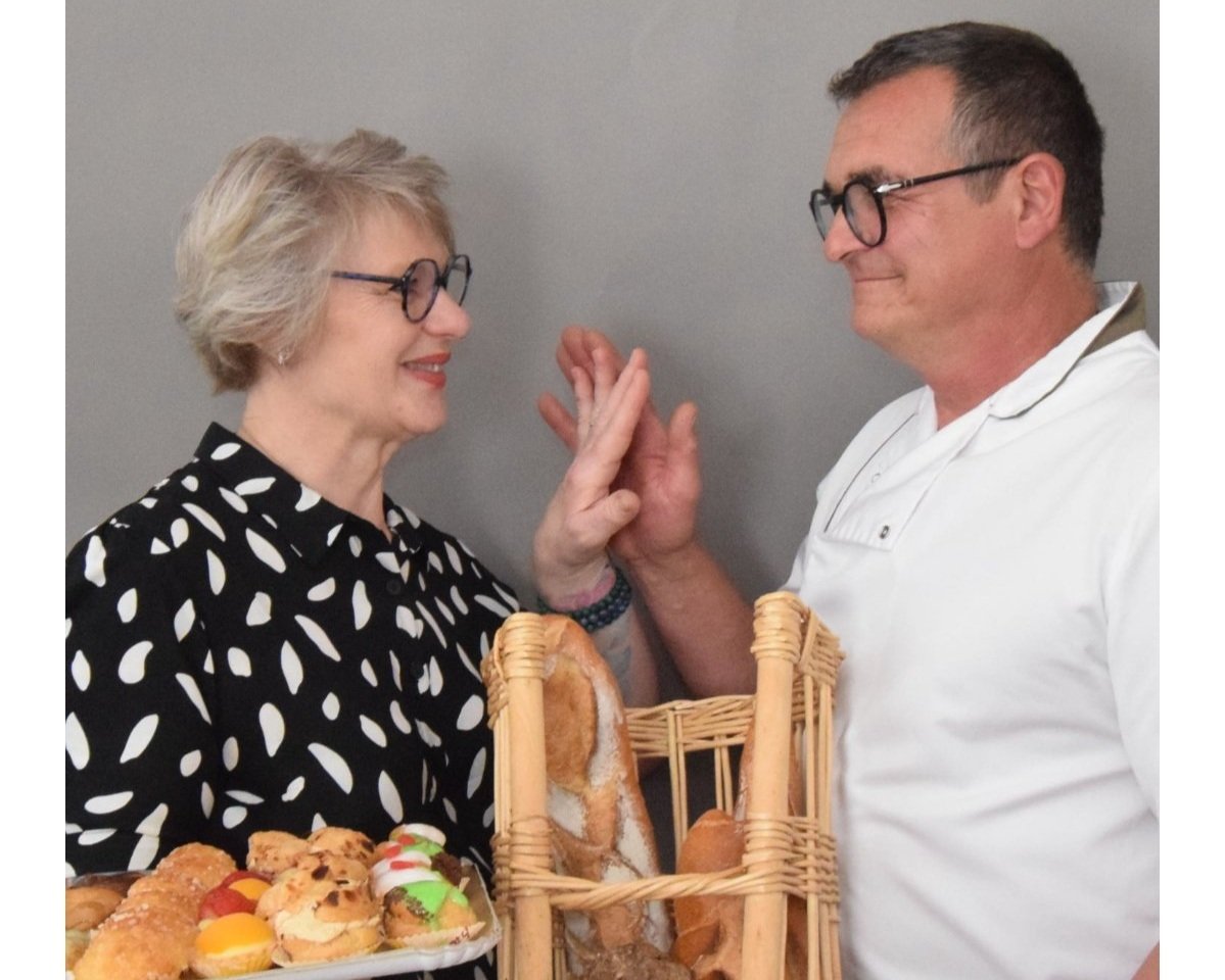Un homme et une femme se sourient, se touchent la main dans un geste d'affection, avec un panier de pain entre eux, et un plateau de pâtisseries devant eux.