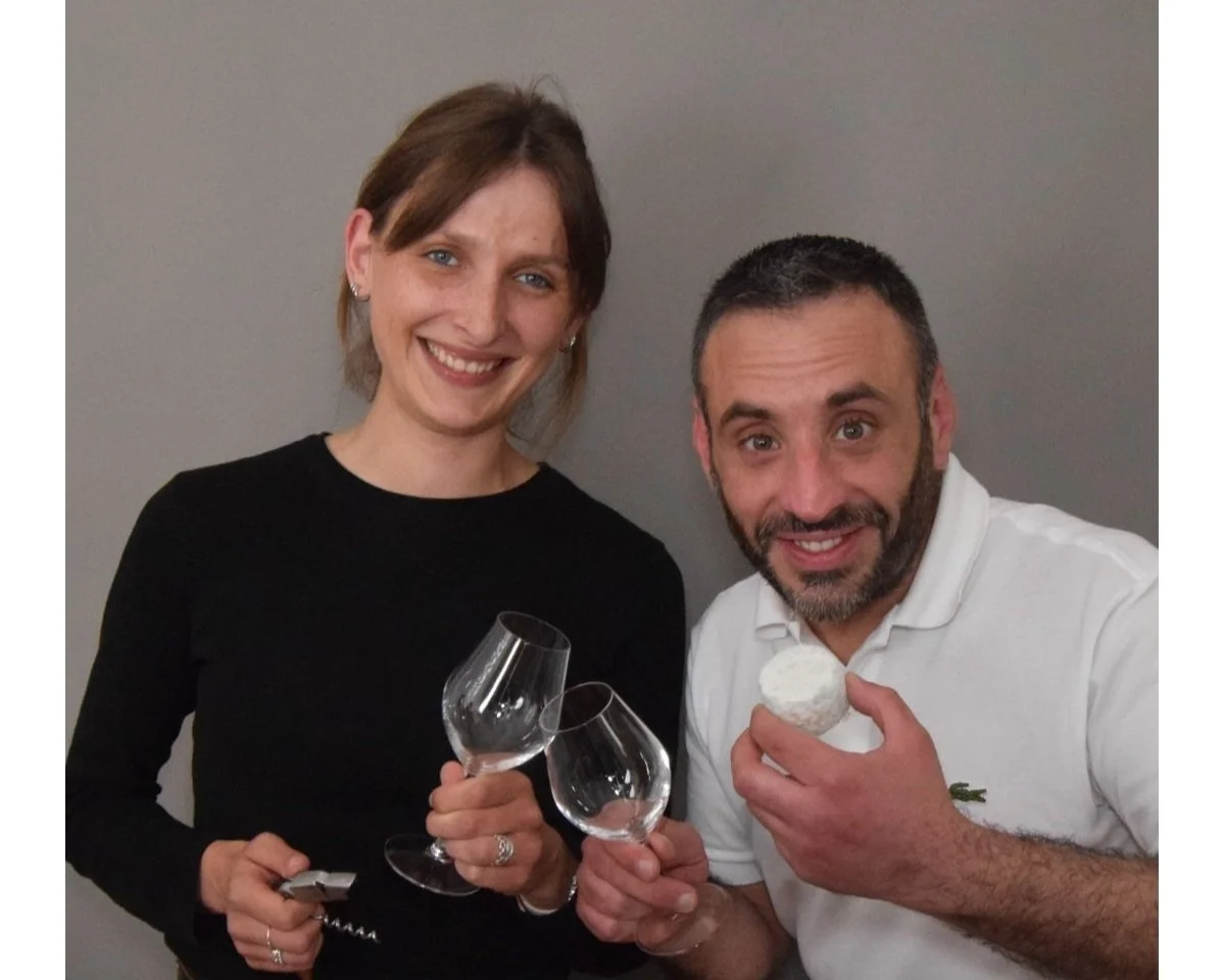 Une femme et un homme souriants, tenant des verres à vin et un cupcake, dans un cadre intérieur.