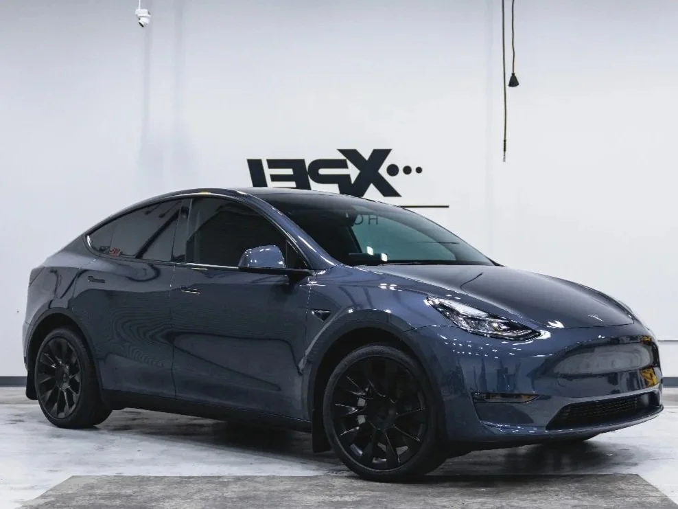 Dark blue Tesla Model Y inside a premium workshop environment in Campbell, showcasing ceramic window tint and paint protection film services by Enthusiast Auto Tint for Tesla and luxury EV protection.
