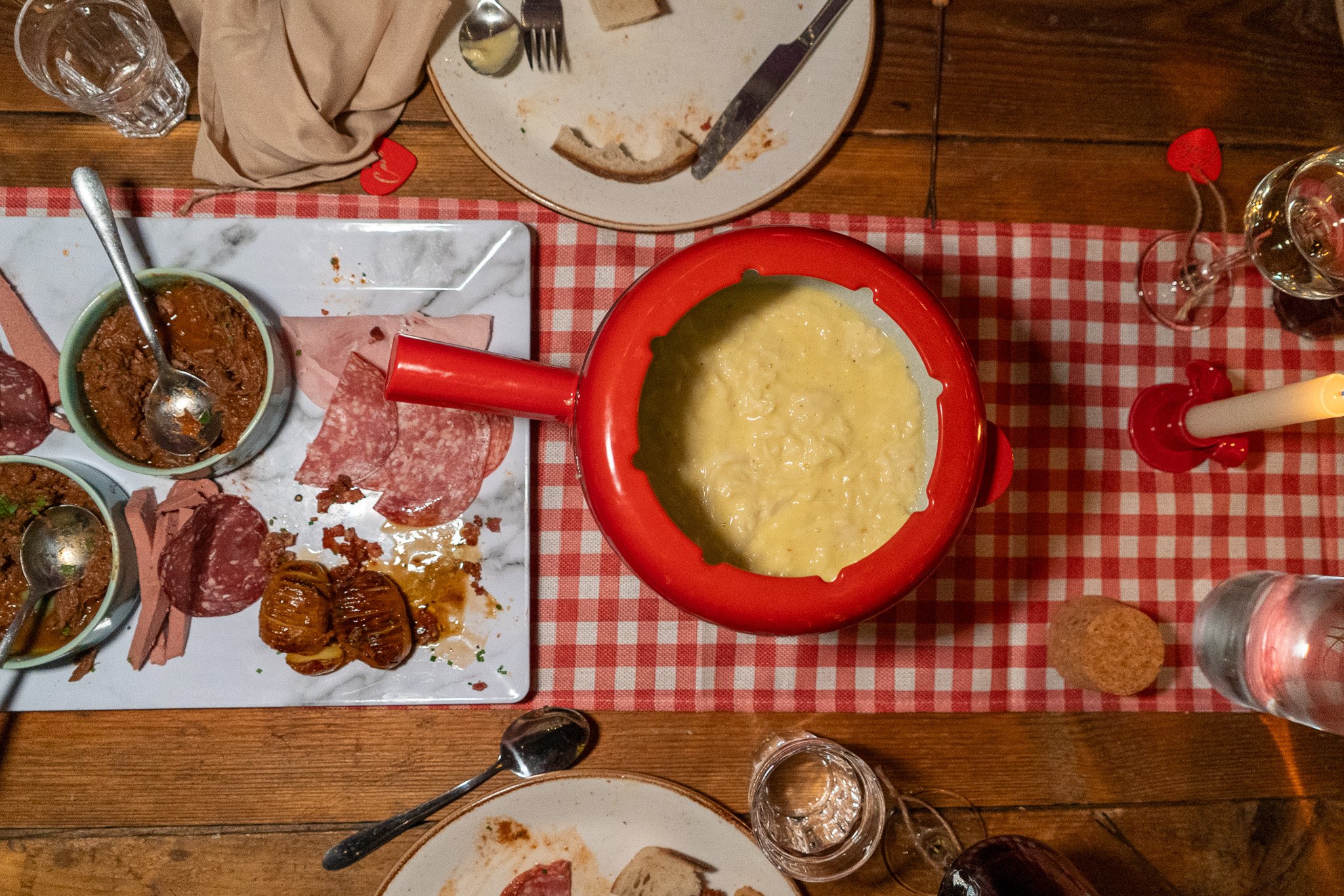 Topt view of a wooden table with a red and white checkered tablecloth in Torrie Barn near Callander. In the center, there is a red fondue pot filled with melted cheese made by Venachar Lochside.
