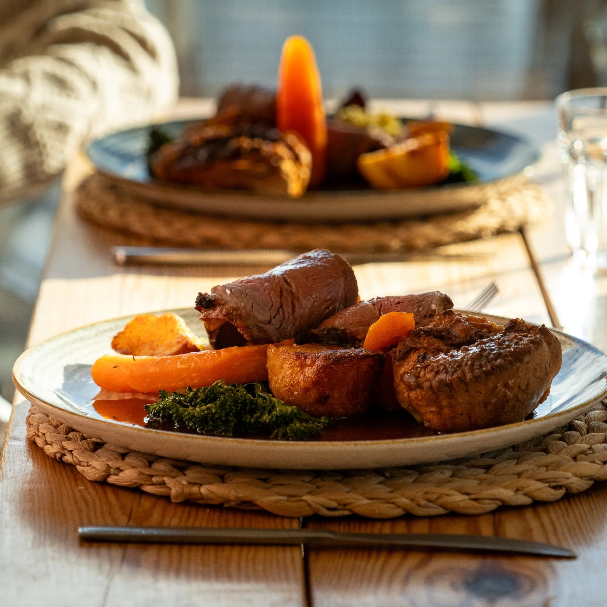 Plate of cooked beef, roasted potatoes, carrots, and broccoli on a woven placemat.