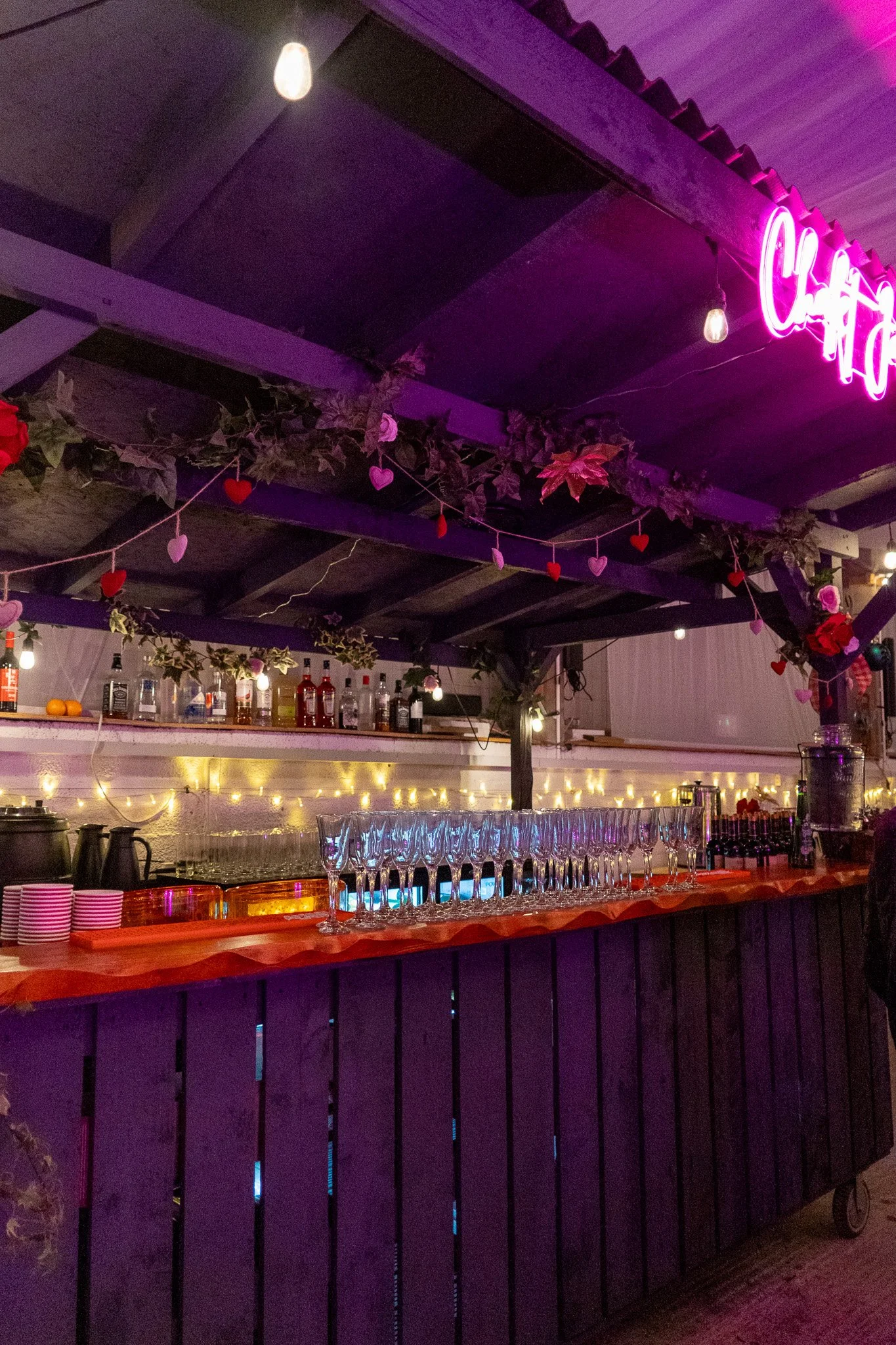 The bar at Torrie Barn decorated with fairy lights, heart-shaped hanging ornaments, and greenery. The setting has a festive and romantic atmosphere with purple and pink lighting.