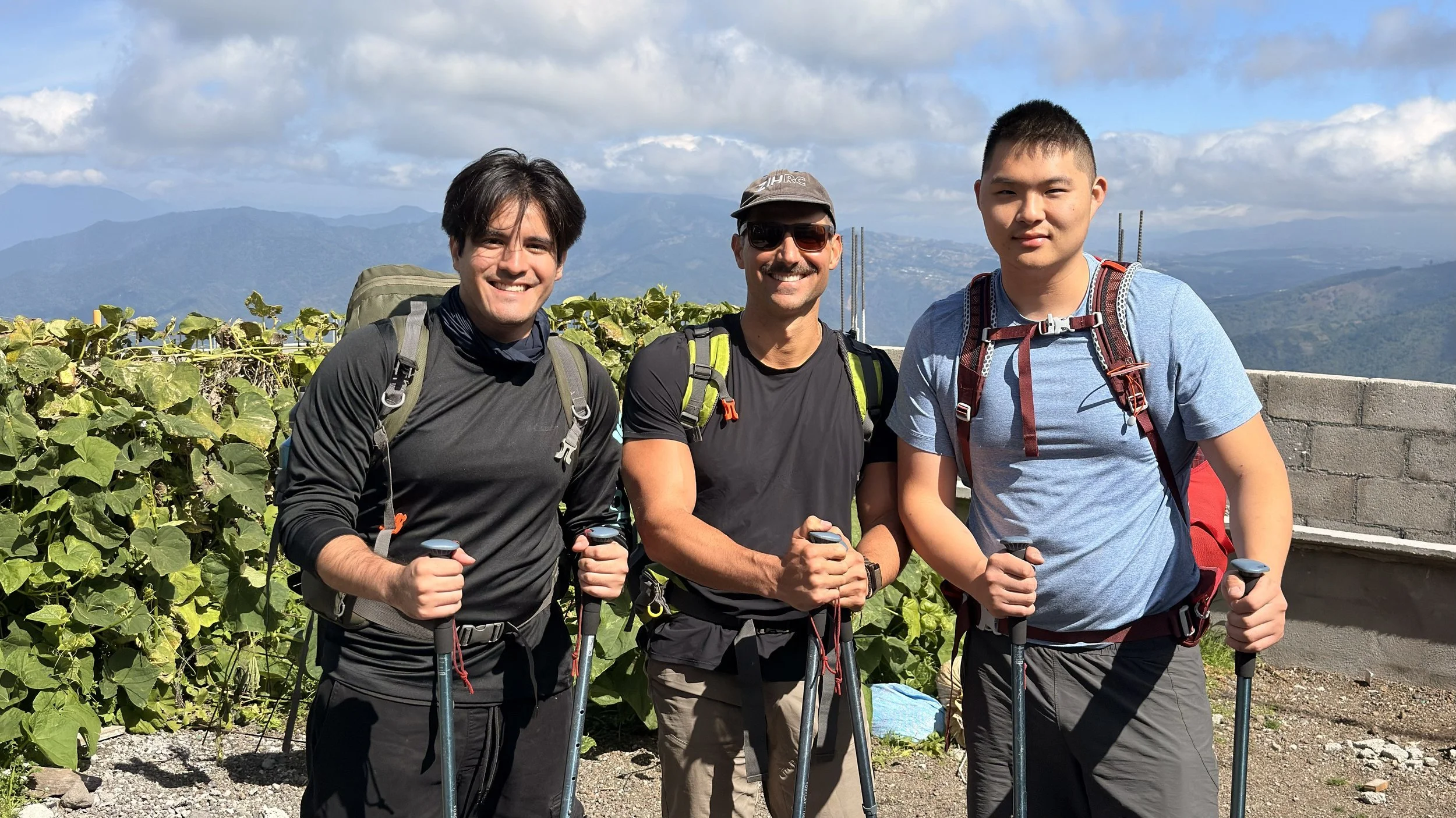 Three hikers with trekking poles at the Acatenango volcano trailhead in Soledad, Guatemala