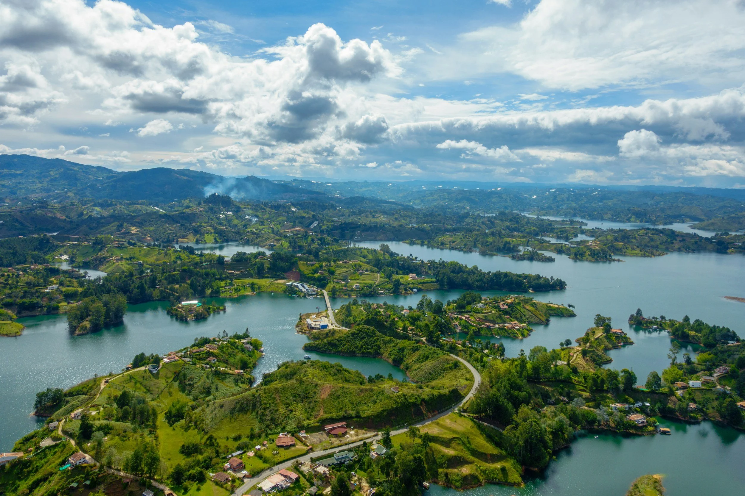 Aerial view of a scenic landscape with lakes, green hills, scattered houses, and a partly cloudy sky.