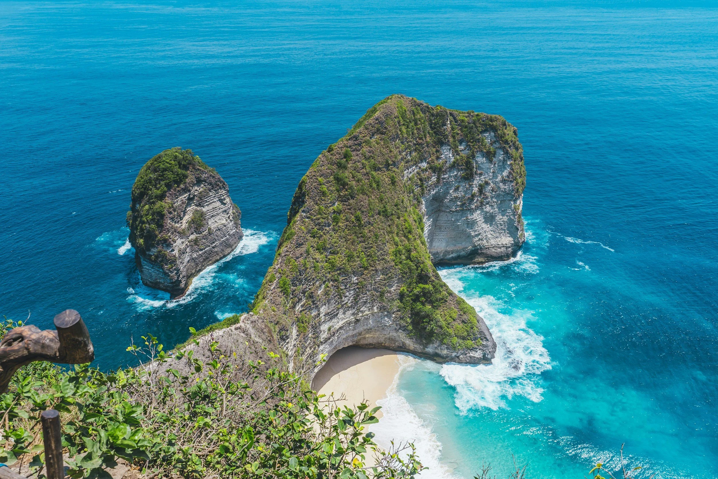 Aerial view of Kelingking Beach on Nusa Penida Island, featuring towering green cliffs, a turquoise cove, and a sandy beach.