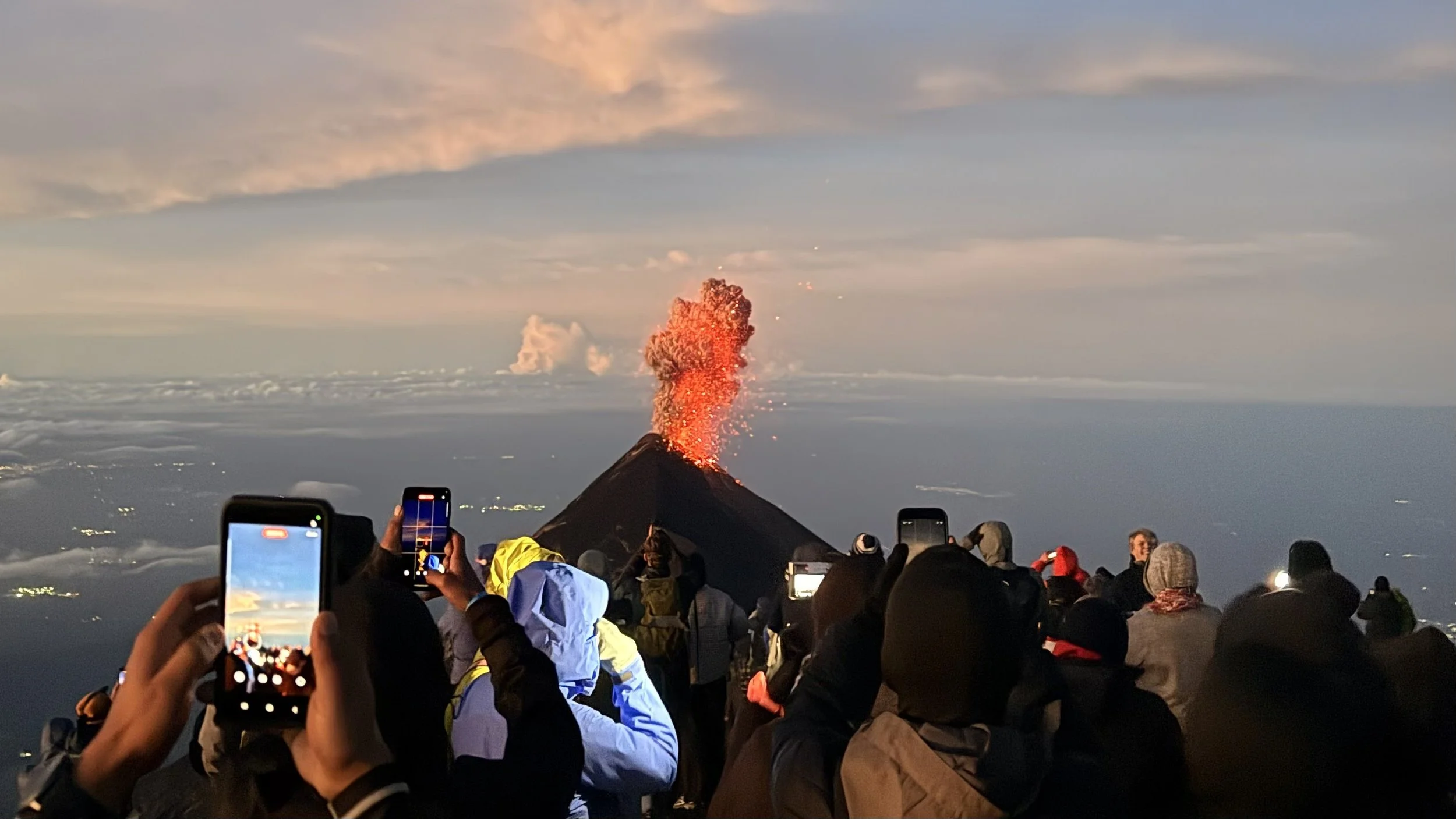 Hikers photographing Volcán de Fuego erupting at sunrise from the summit of Acatenango, Guatemala
