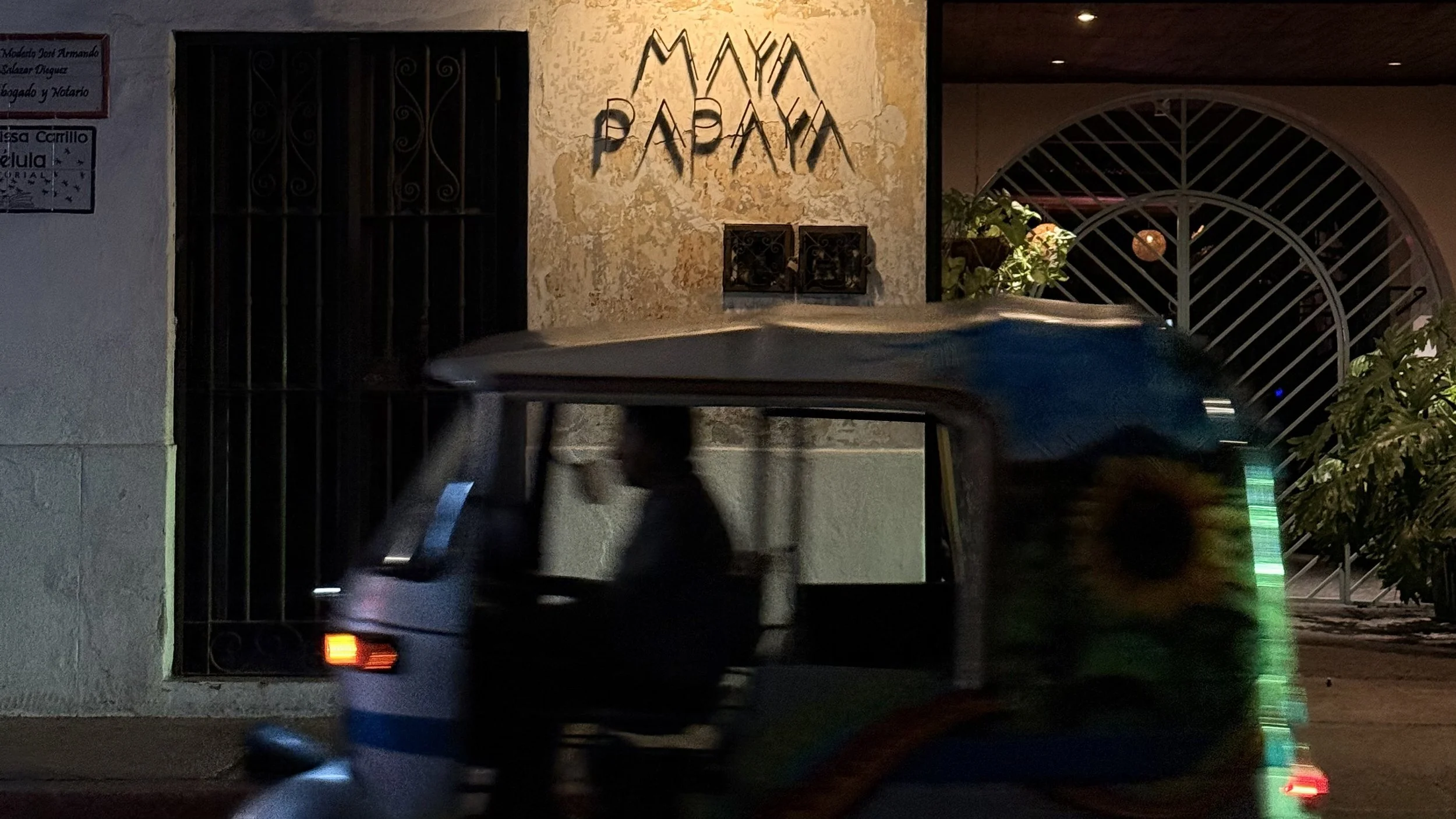 Tuk-tuk passing the Maya Papaya storefront at night in Guatemala