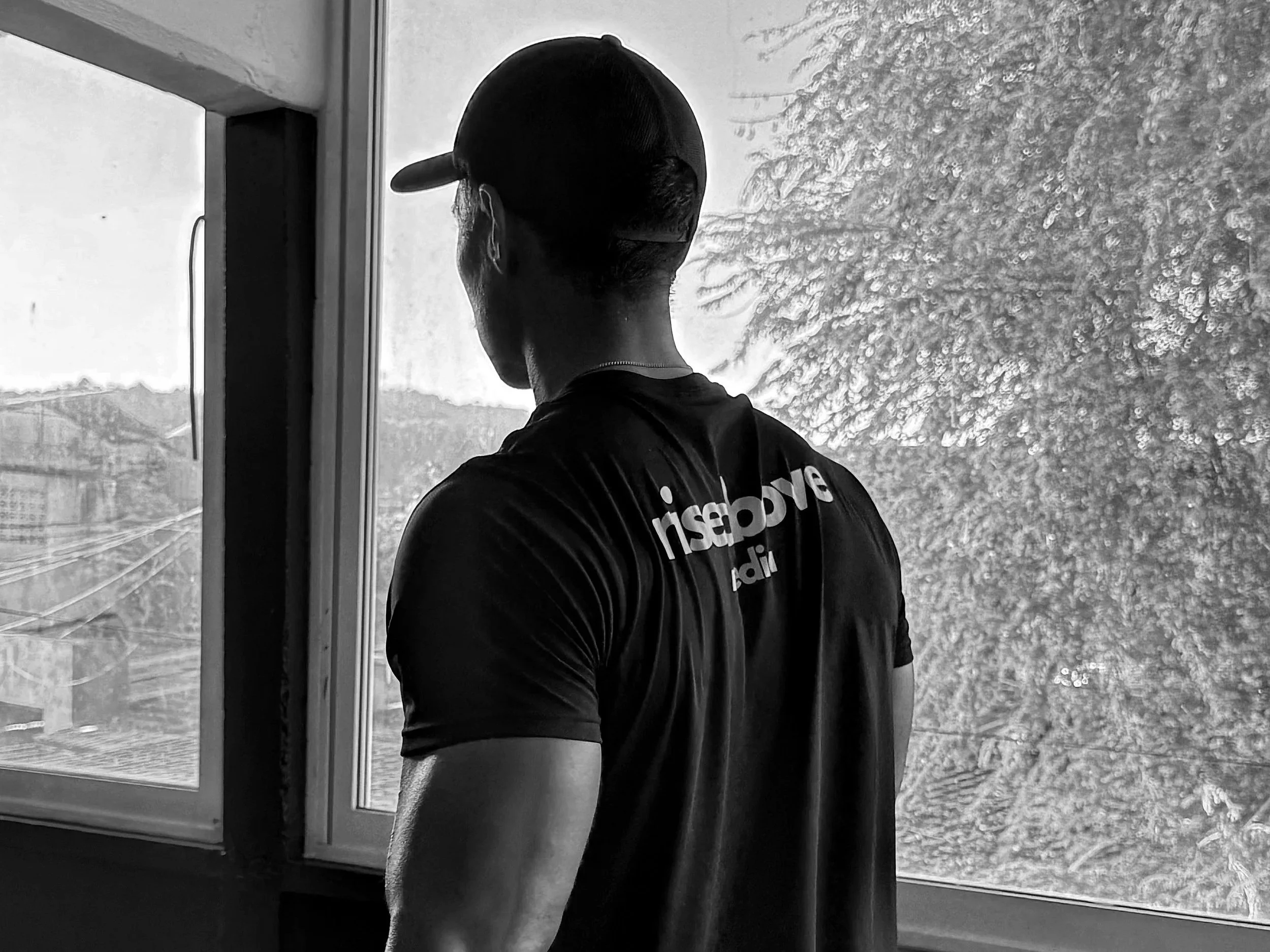 Black and white image of man in gym with shirt that says rise above media.