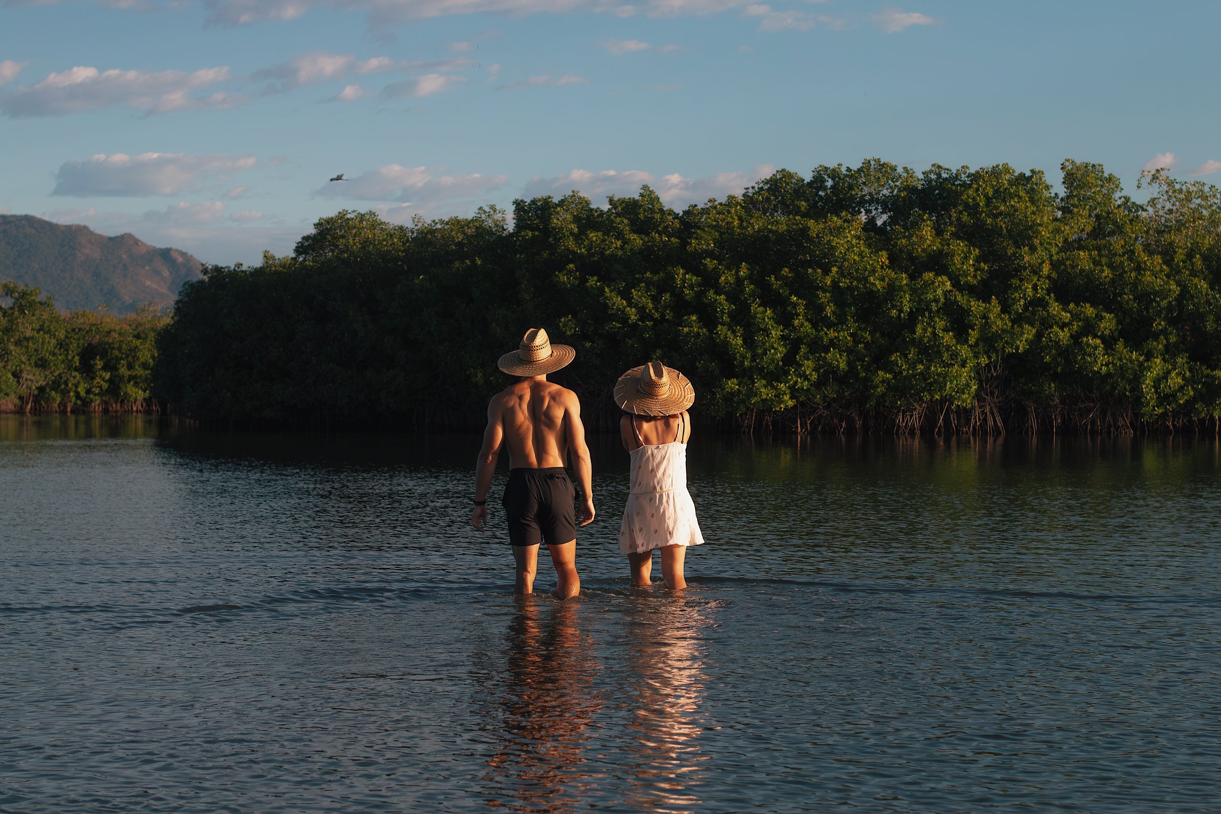 Buff man and woman with backs facing standing in lagoon in zihuatanejo mexico
