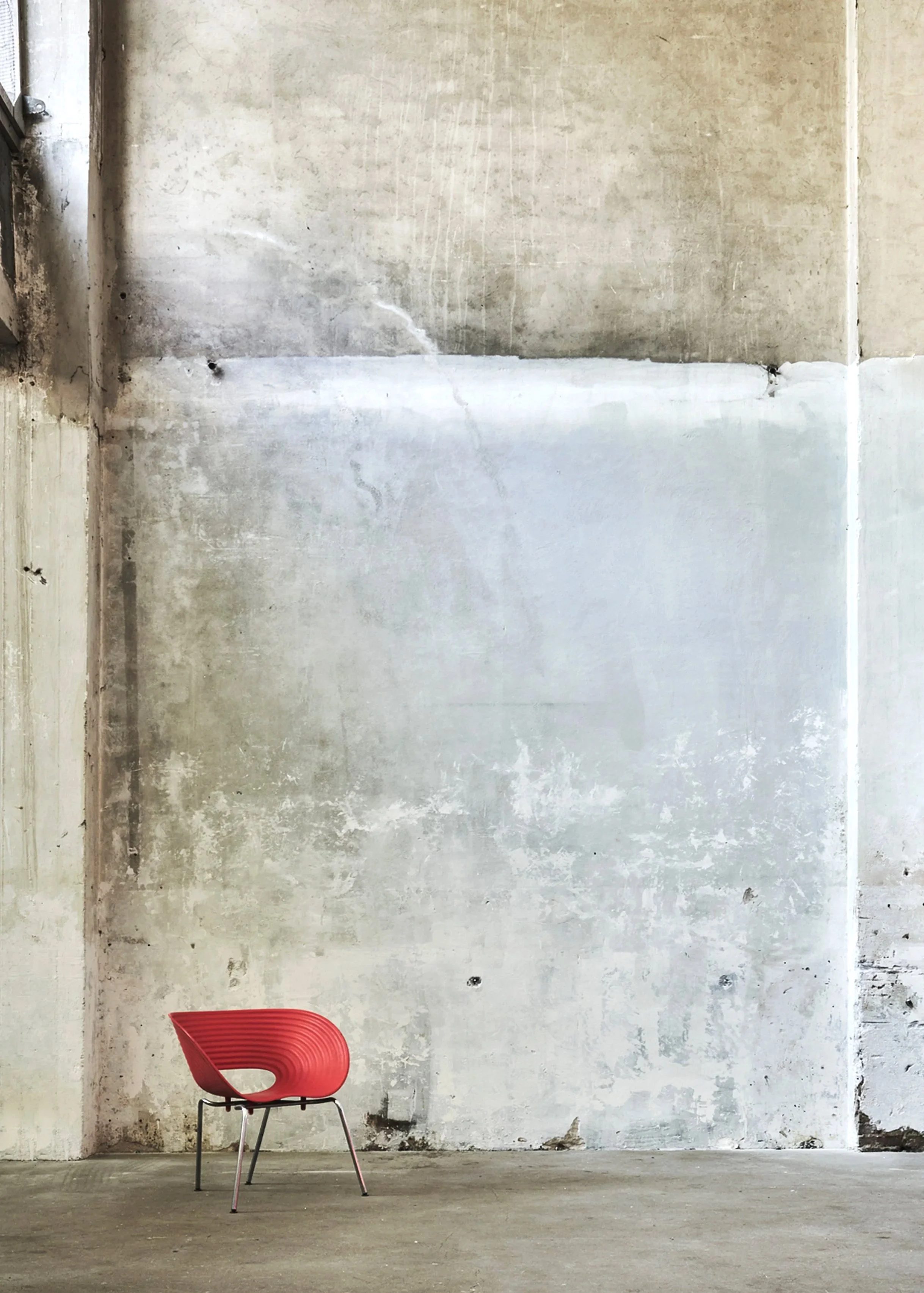 A red modern chair with metal legs placed against a worn, industrial-style concrete wall | Rental Studio for Film, Photography and Events | Hembrug Zaandam | Greater Amsterdam