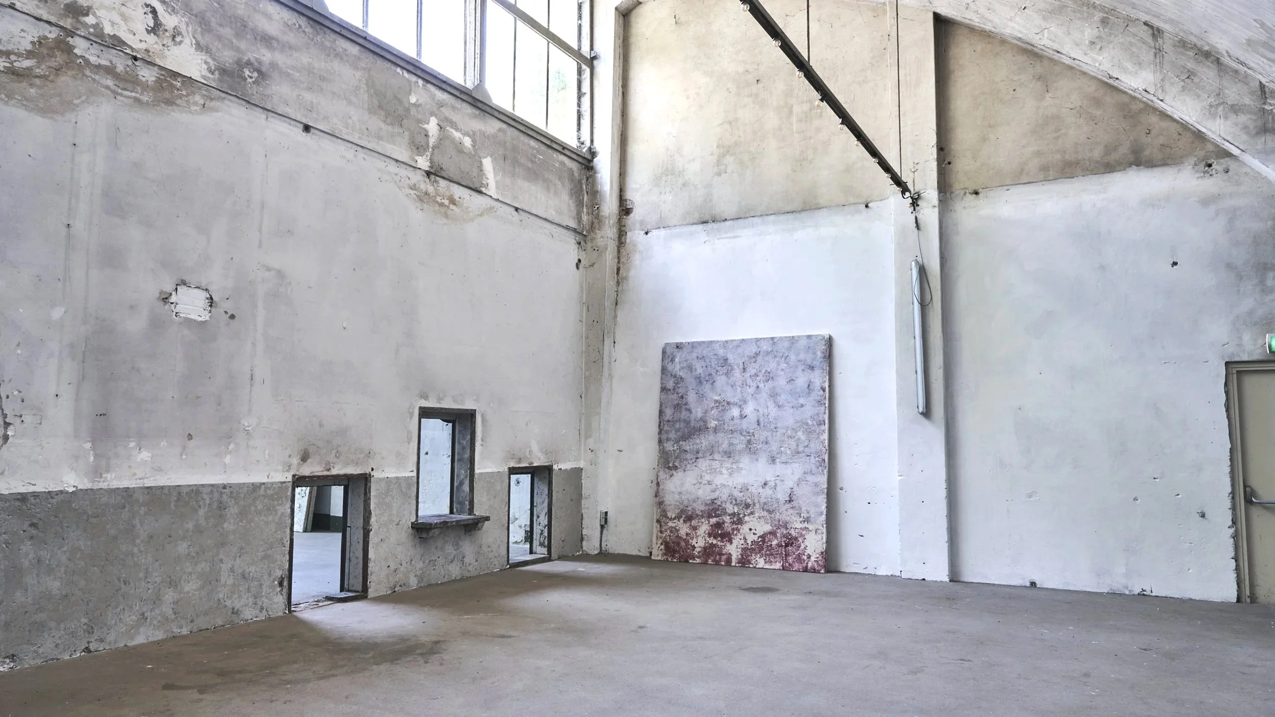 Empty industrial space with high ceilings, large windows, and concrete walls, with an abstract painting leaning against the wall | Rental Studio for Film, Photography and Events | Hembrug Zaandam | Greater Amsterdam