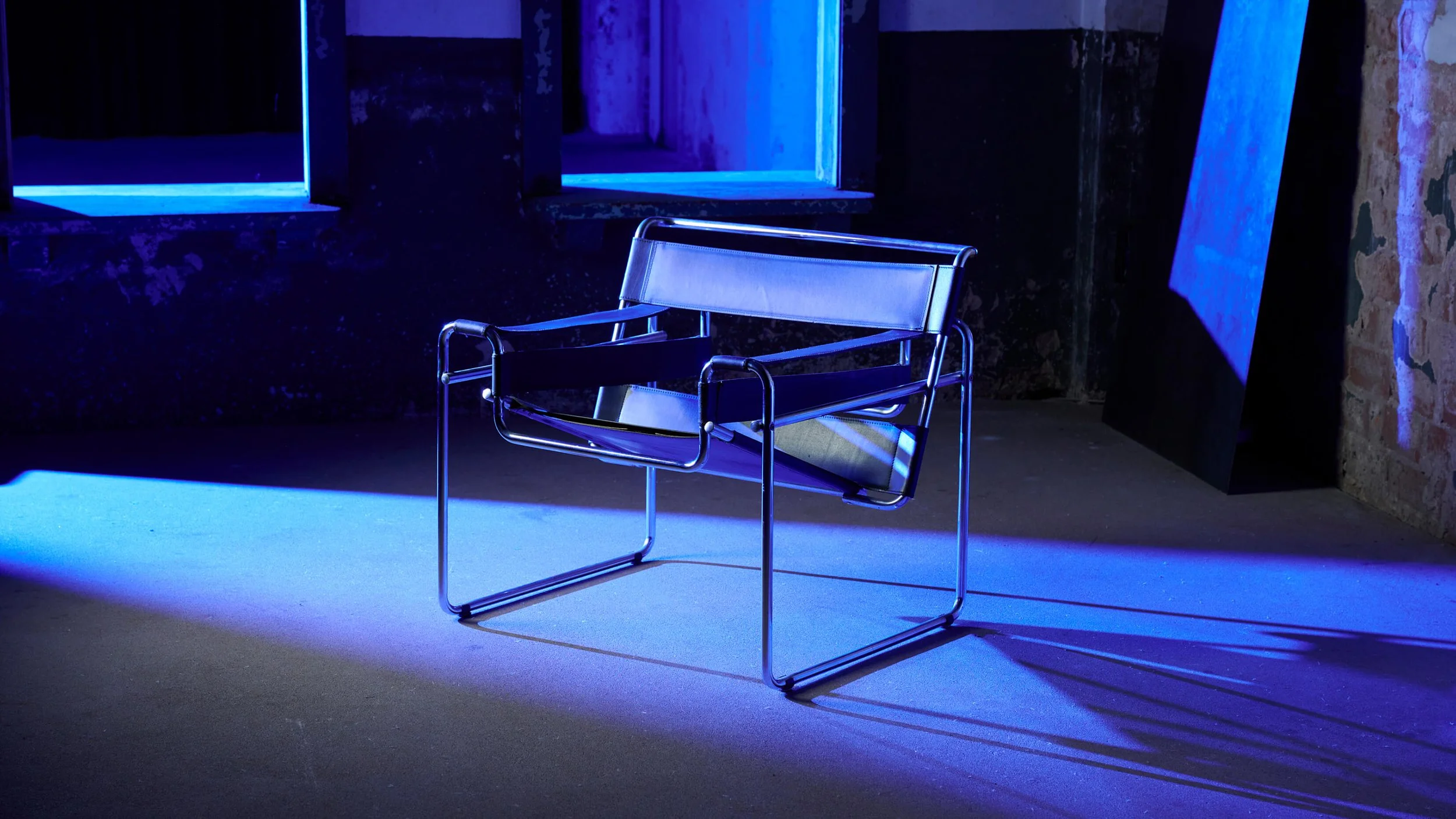 A modern black and chrome chair sitting on a floor illuminated by blue lighting with windows and a brick wall in the background | Rental Studio for Film, Photography and Events | Hembrug Zaandam | Greater Amsterdam