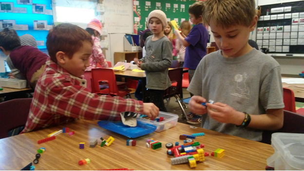 Children in a classroom playing with LEGO bricks at a table.