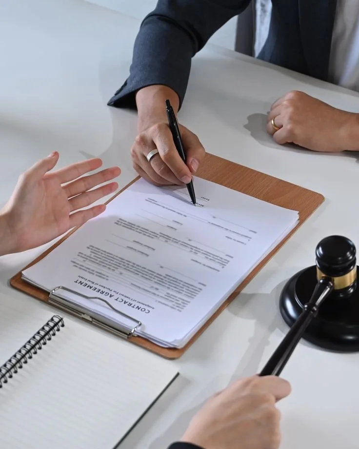 A serene courtyard with a rectangular fountain in the center, surrounded by lush greenery, small trees, and a white wall with black lanterns. There is a black gate in the background, and tall cypress trees and mountain in the distance.