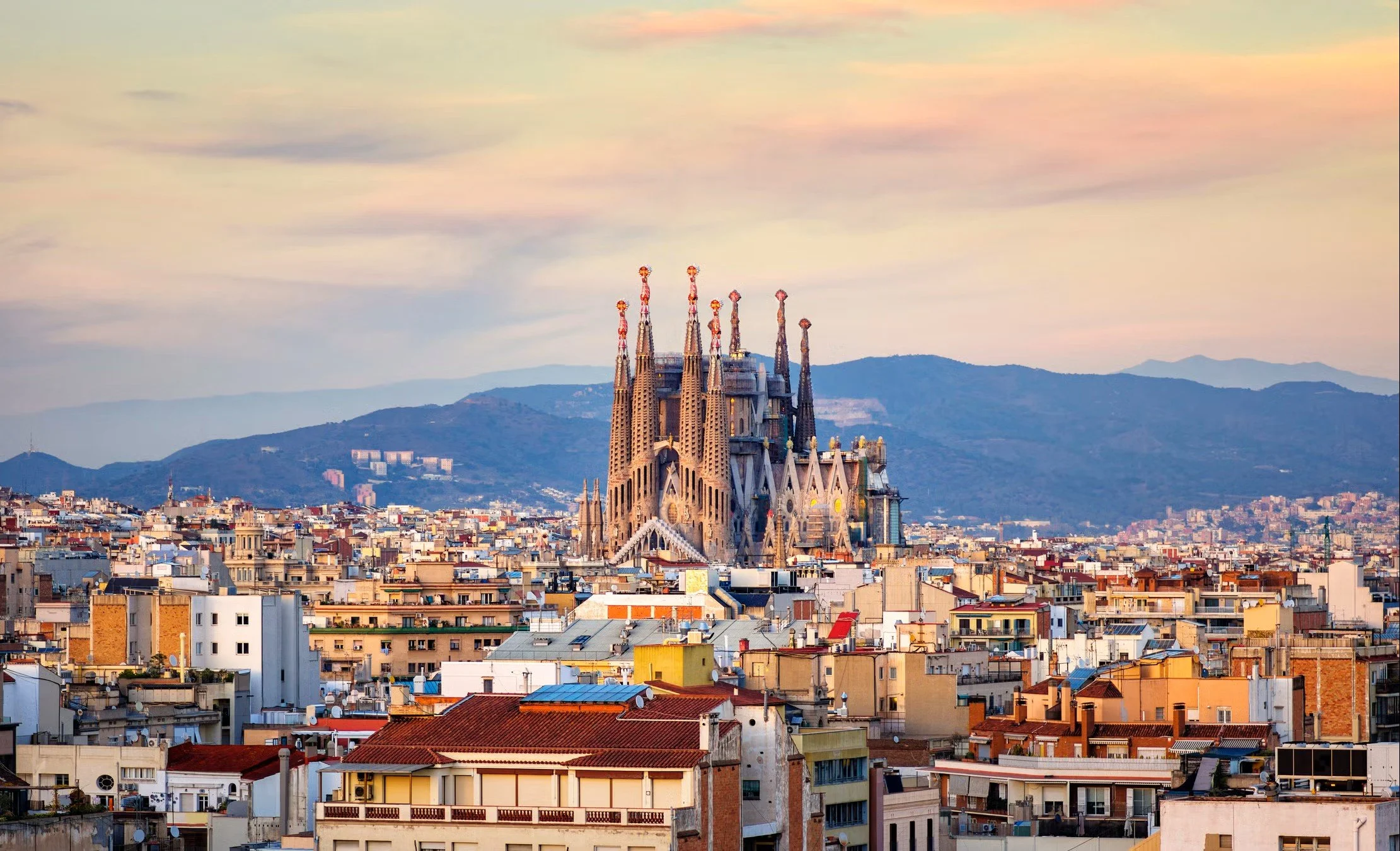 View of Barcelona city skyline with La Sagrada Familia basilica in the center during sunset, with mountains in the background near Barcelona, Spain.