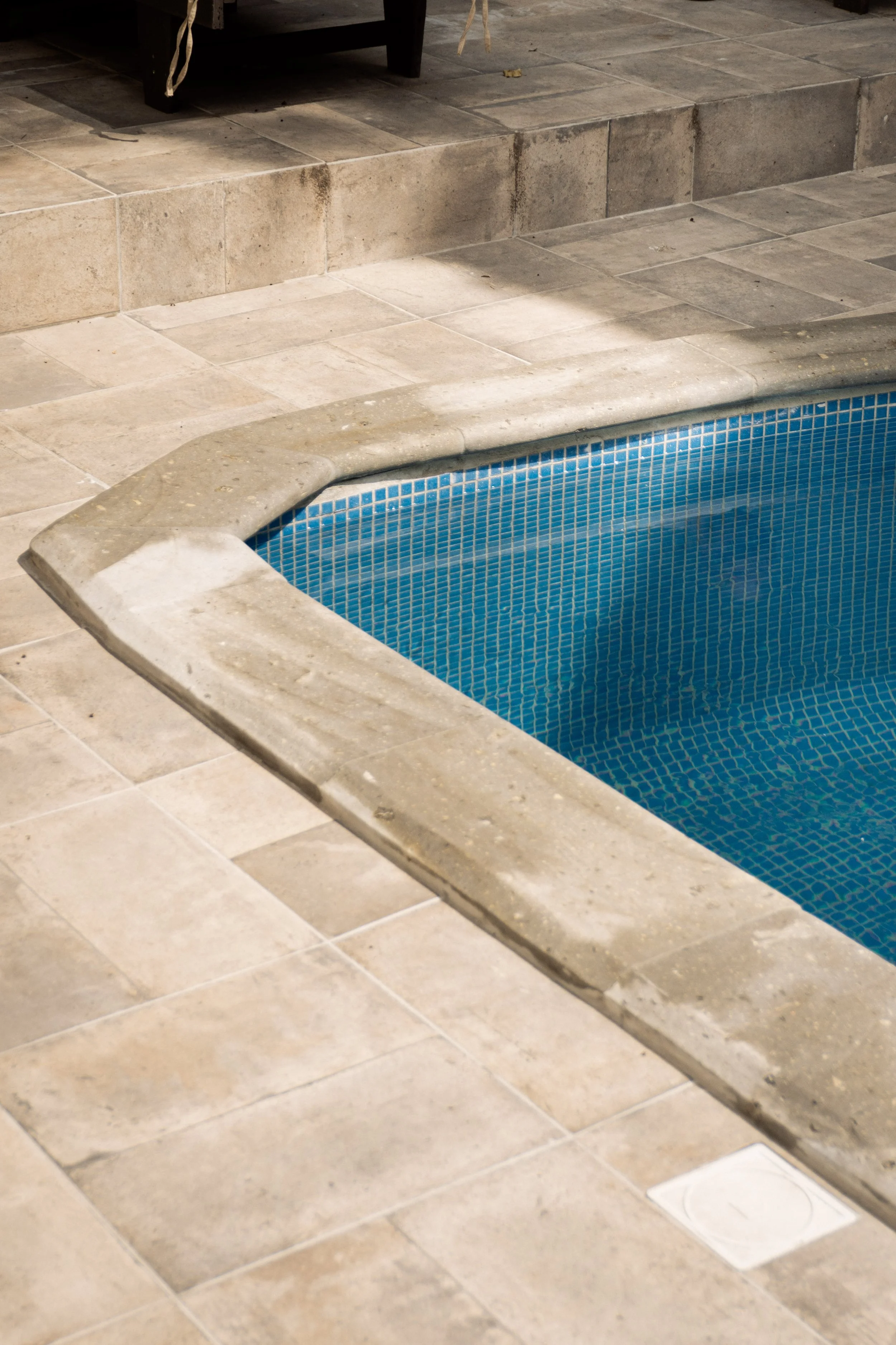 Primer plano de una esquina de alberca con azulejos de piedra beige y pequeños mosaicos azules que recubren el interior de la alberca, con escalones que conducen a la alberca de Polari, el mejor sauna gay de Guadalajara