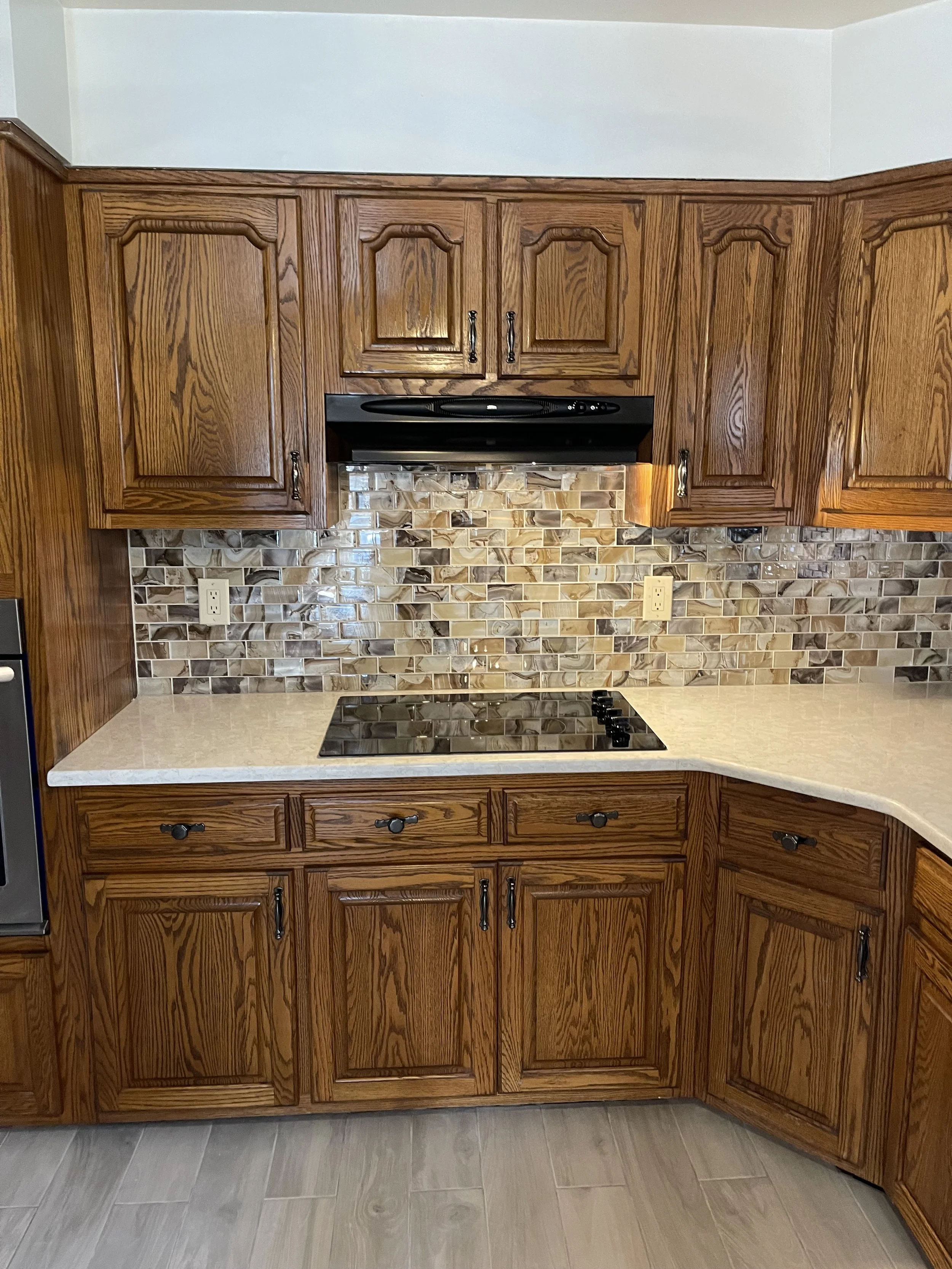Kitchen with wooden cabinets, marble countertop, and multicolored tile backsplash featuring shades of brown, beige, and cream.