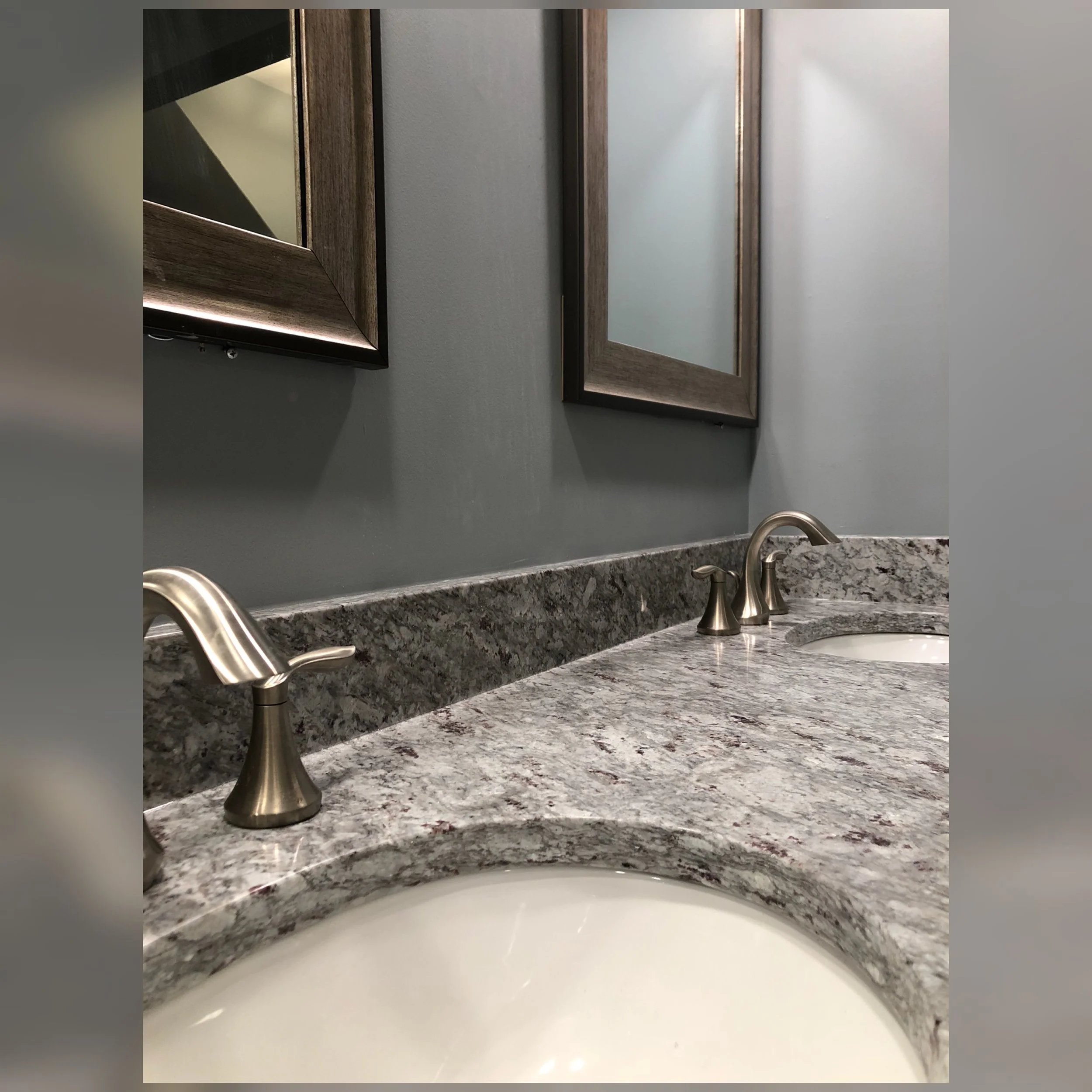 A bathroom with marble countertops, dual sinks, brushed nickel faucets, and framed mirrors above the sinks.