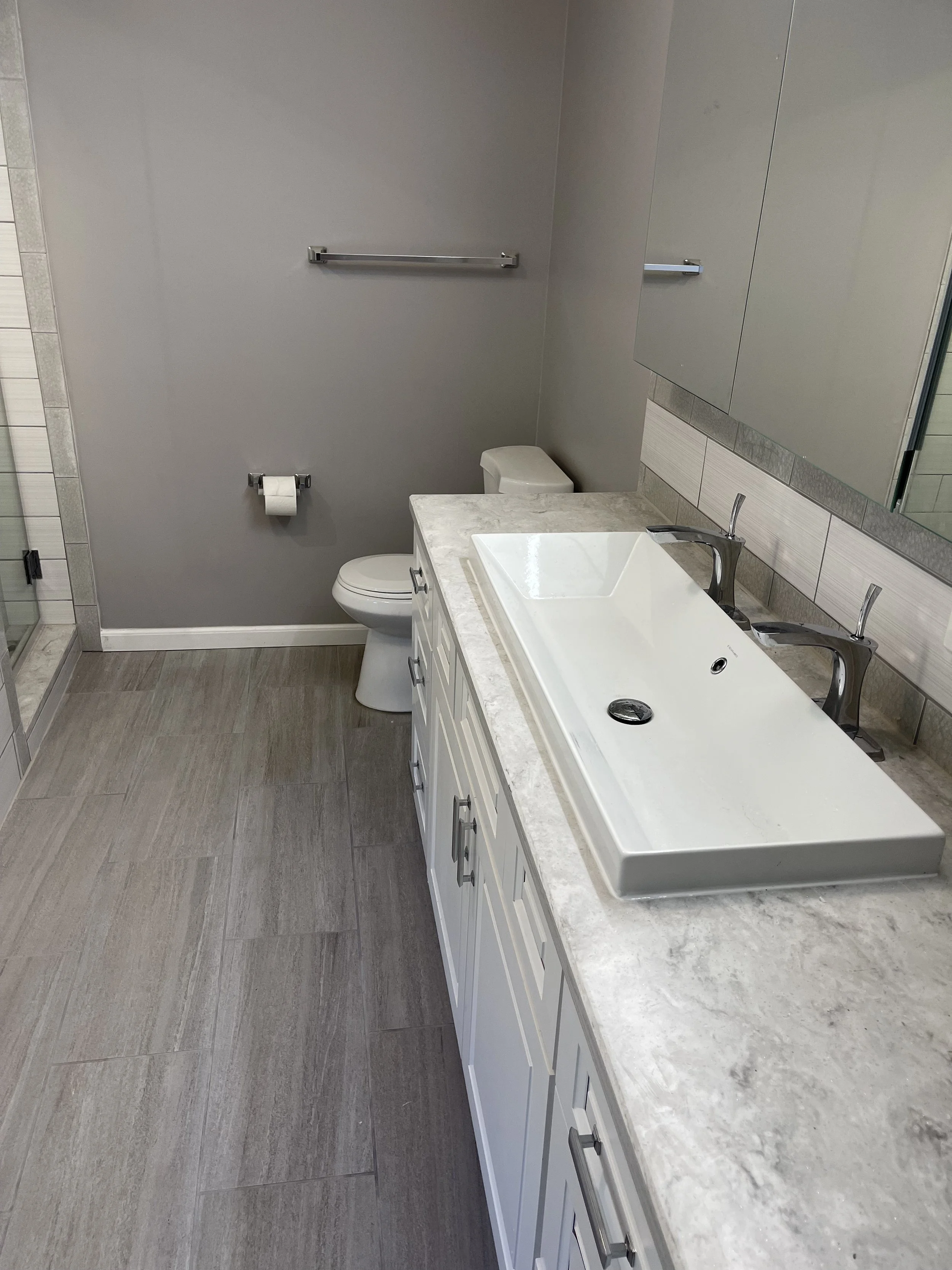 Bathroom with a gray wall, a white toilet, a towel bar, a countertop with a rectangular vessel sink, and a large mirror above the sink.