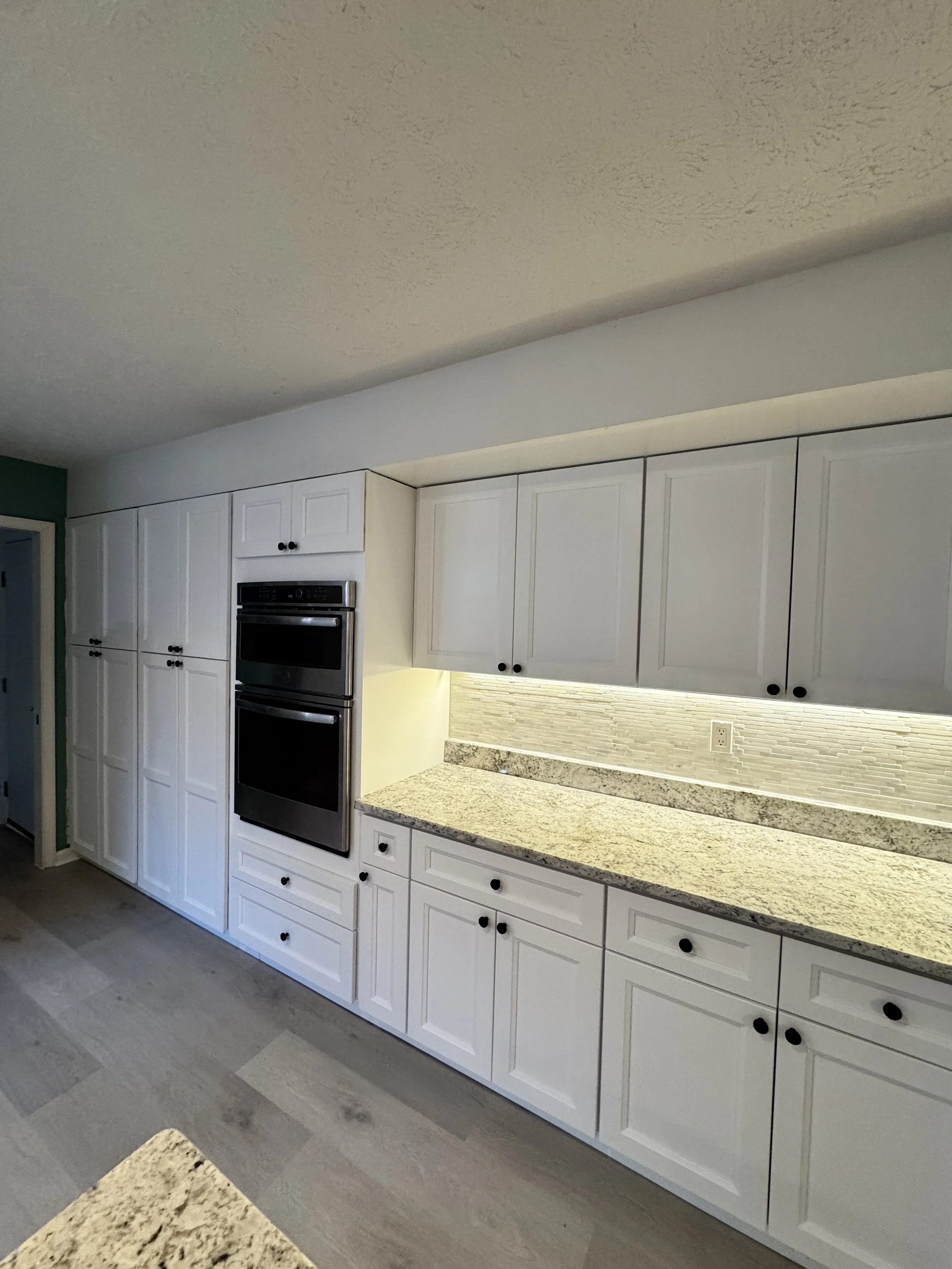 Kitchen with white cabinets, granite countertops, and built-in double oven.