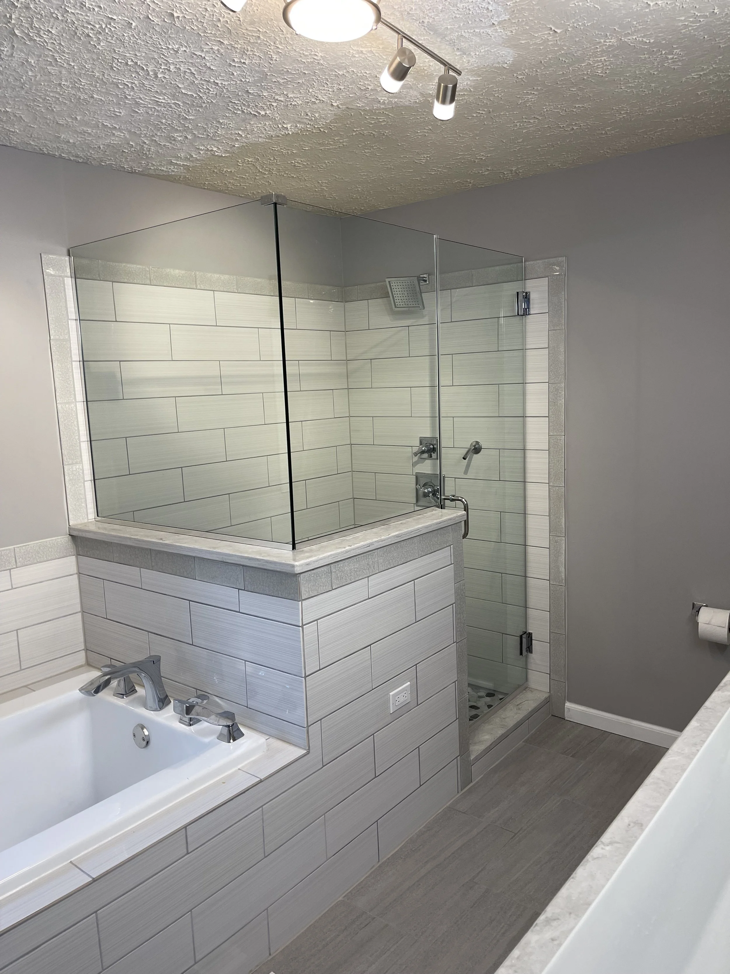 Bathroom with a corner shower stall with glass panels, a bathtub with silver fixtures, and gray tiles and walls.