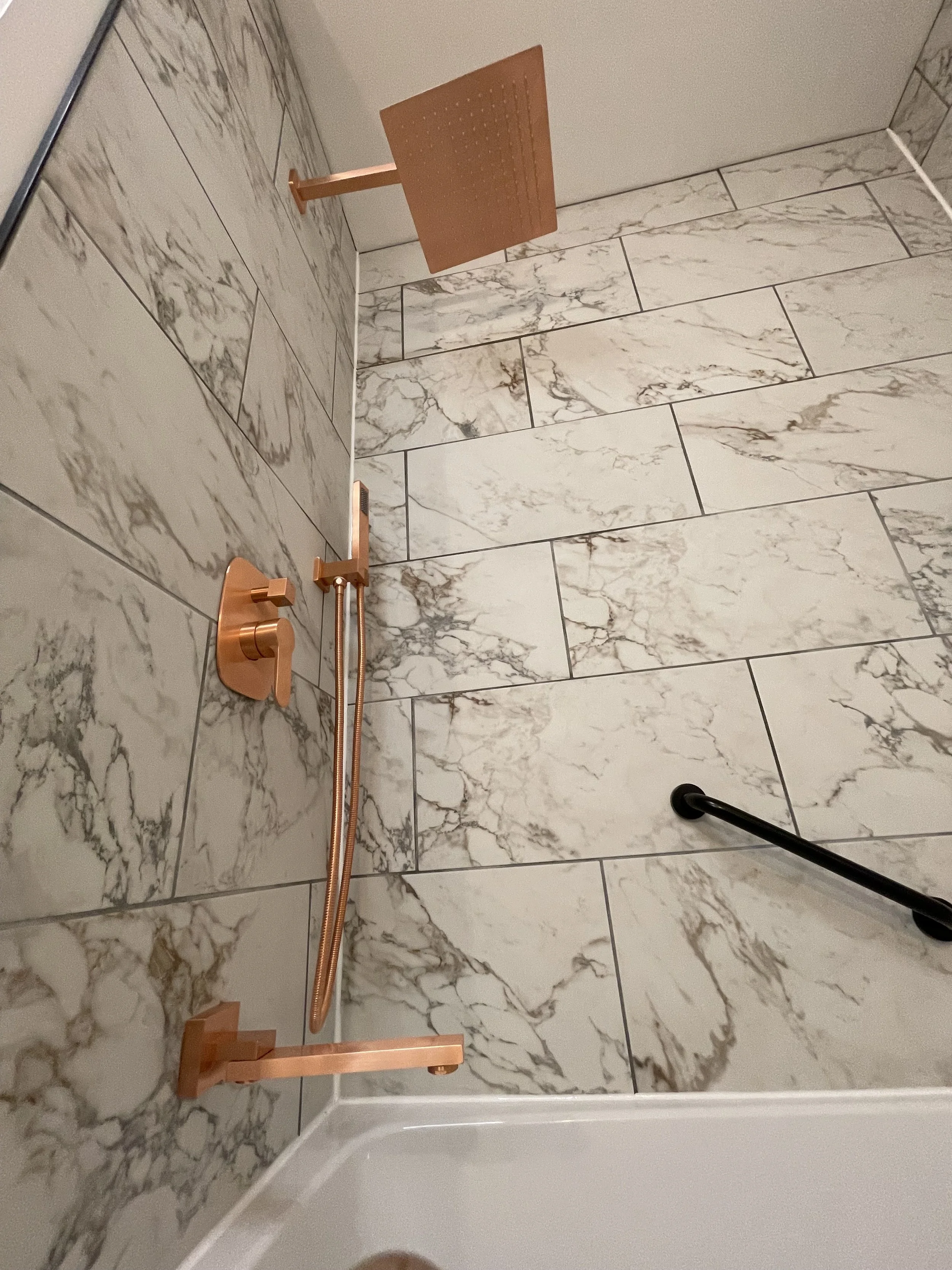 Shower with copper fixtures, a square copper showerhead, and marble tile walls.