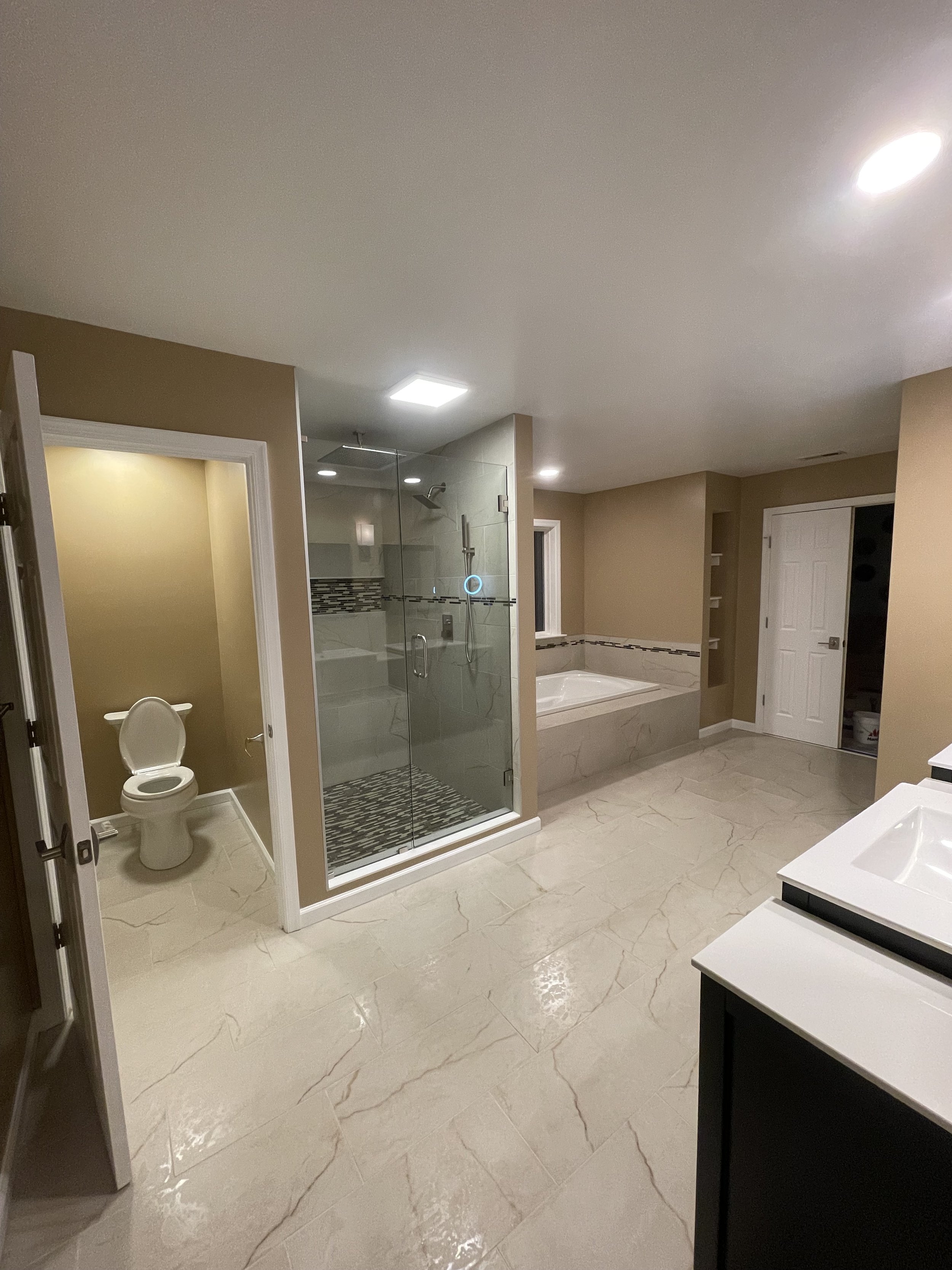 Modern bathroom with a glass-enclosed shower, a bathtub, a toilet, and dual sinks with white countertops.