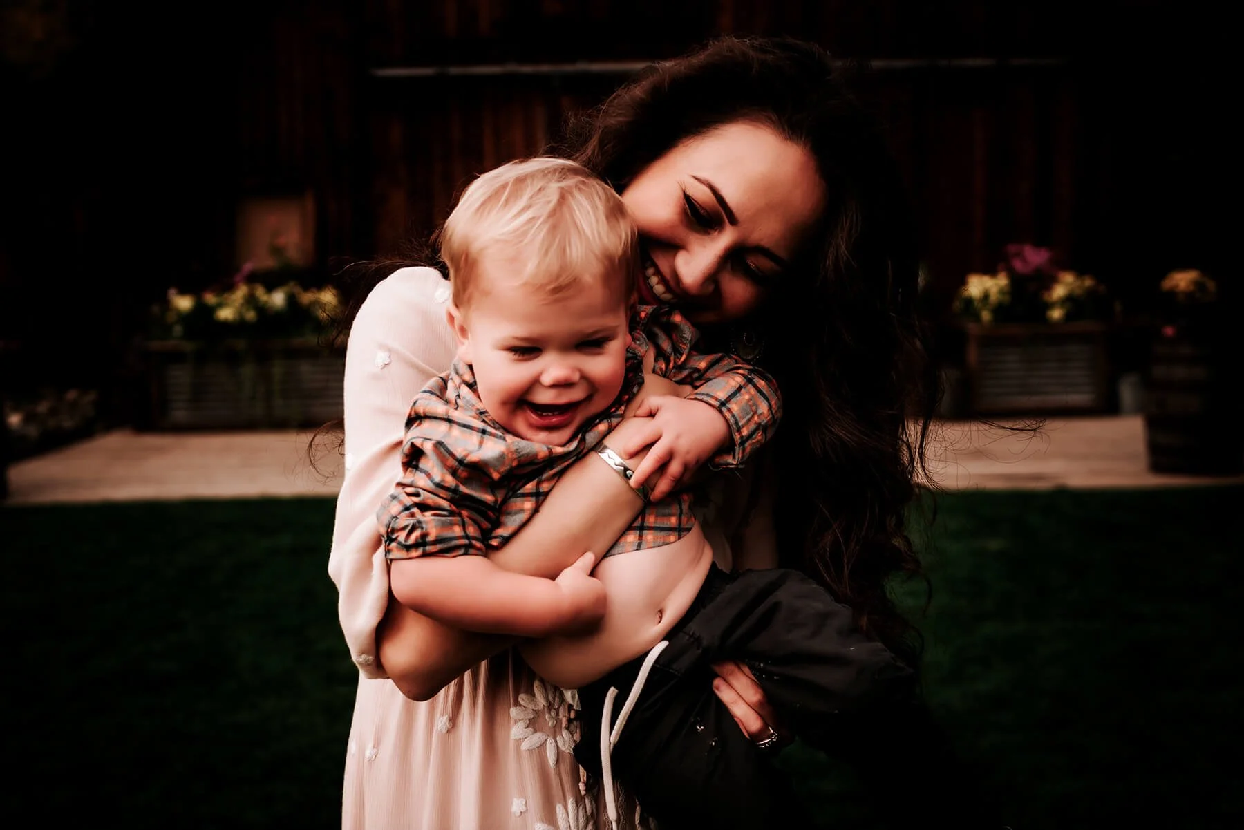 A woman with long dark hair holding a smiling young boy with blond hair outdoors at night.