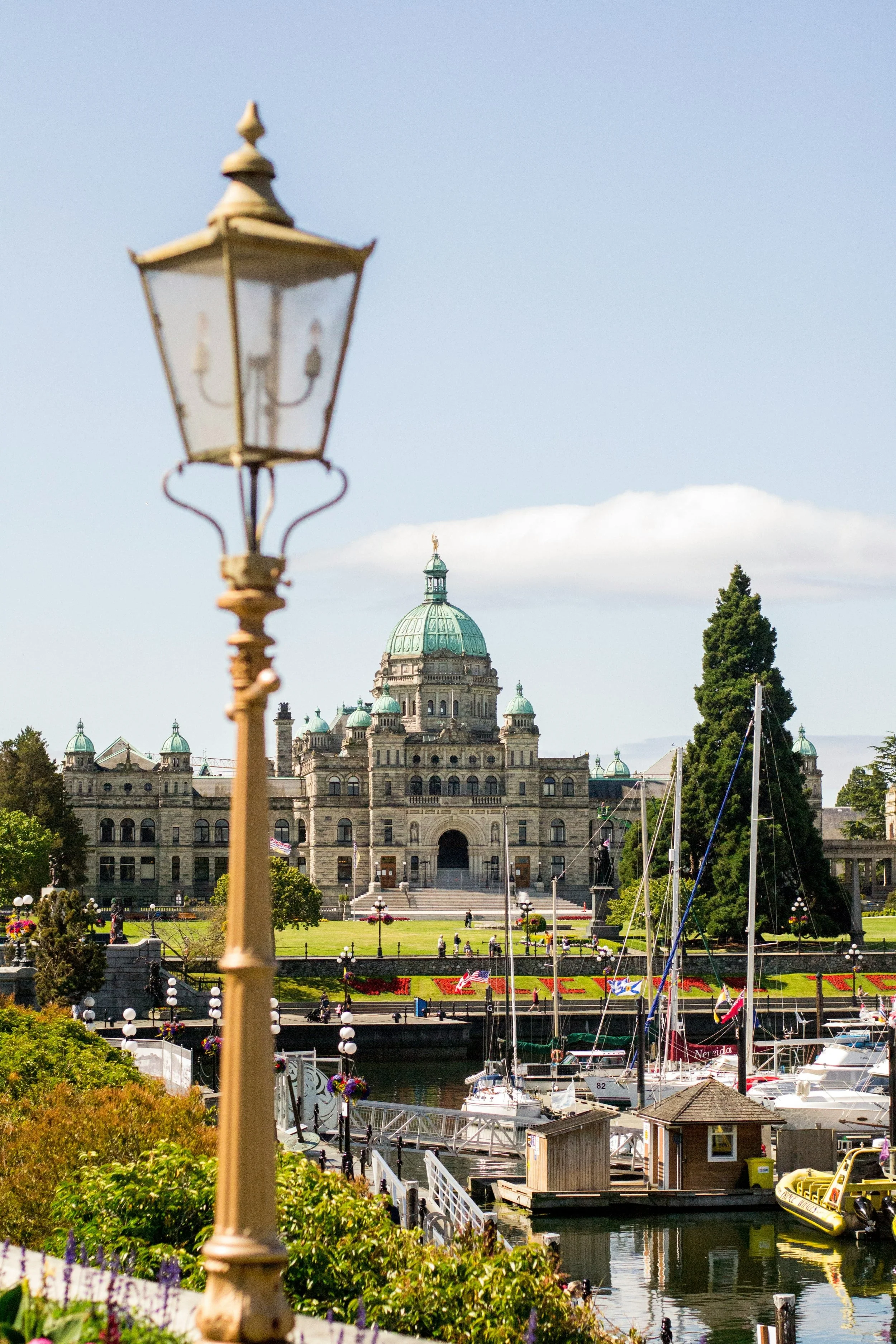 A harbor with boats, colorful flowers, and old-fashioned lamp posts, with a historic government building with a green dome in the background.