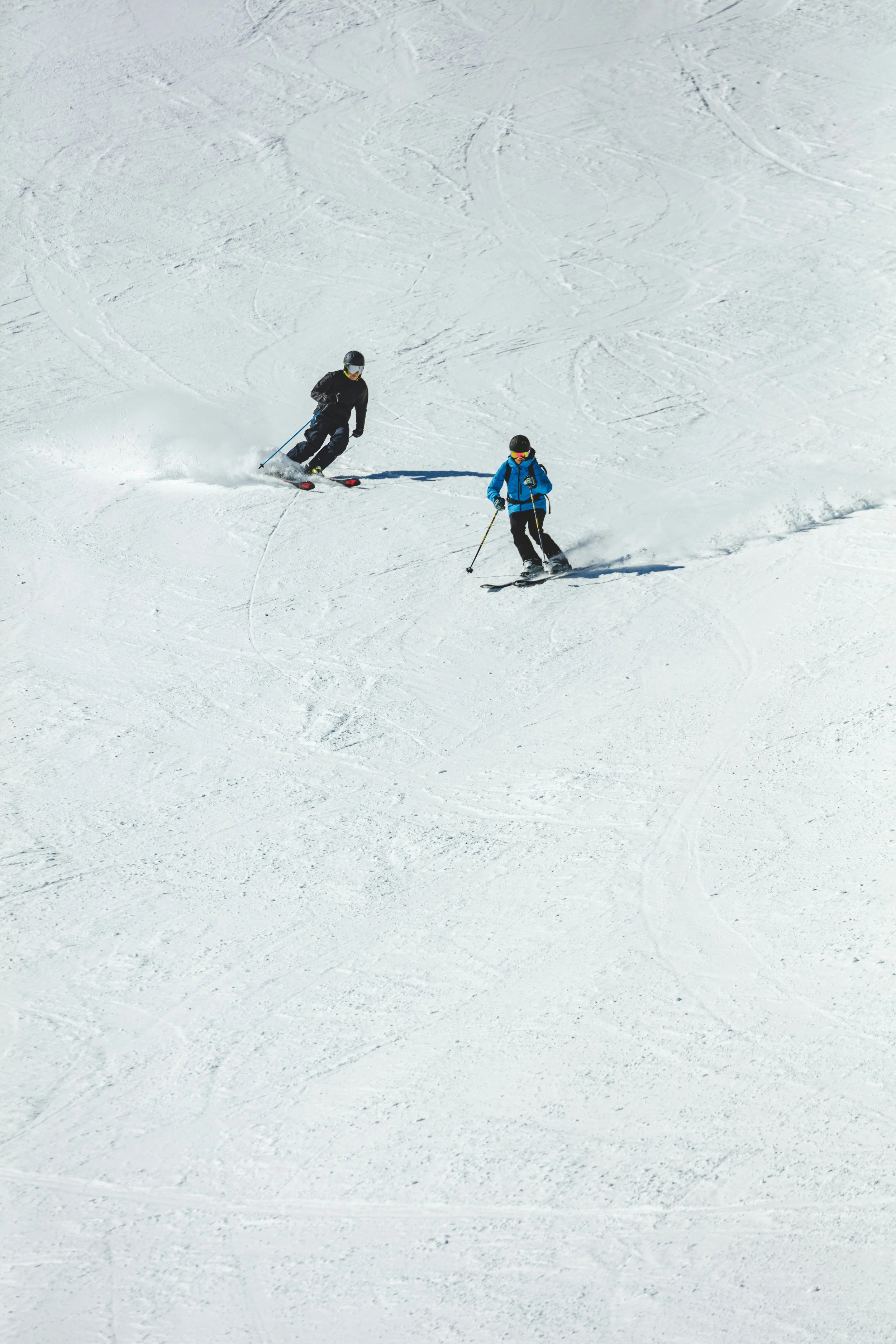 Two children skiing down a snow-covered slope on a bright, sunny day.
