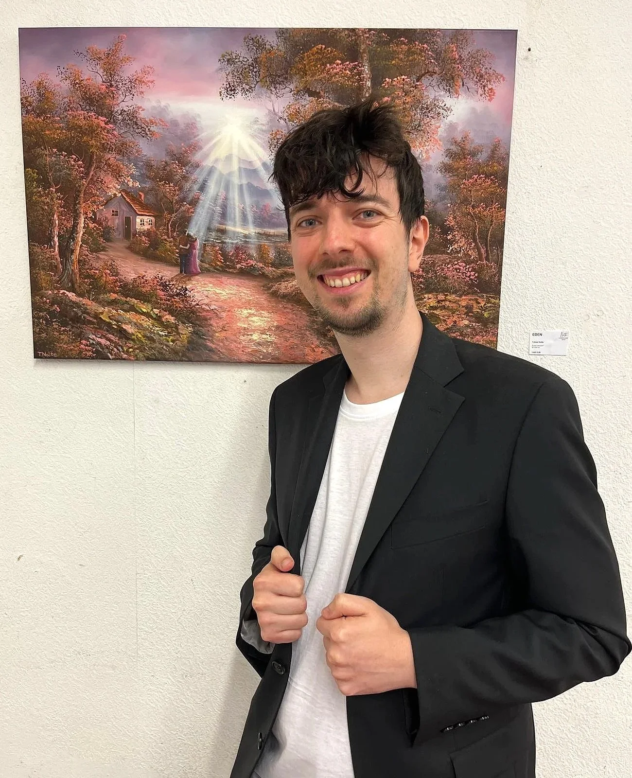 Tobias Nolte präsentiert sich in einem schwarzen Anzug neben einem seiner Gemälde.