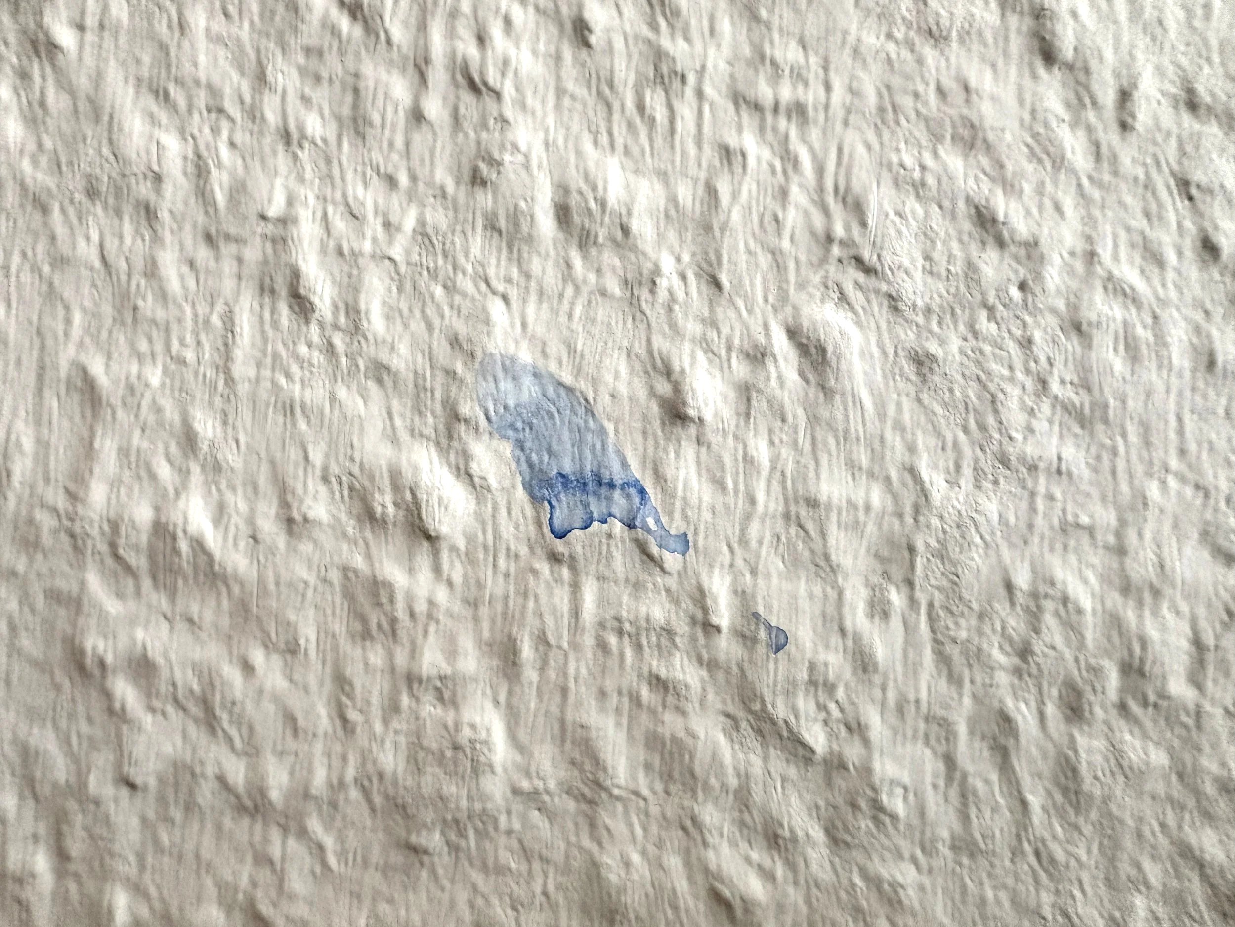 Blauer Farbfleck auf einer weißen Wand neben einer Staffelei. Eine sichtbare Erinnerung an emotionale Überforderung während einer kreativen Blockade und den Weg zu einer gesünderen Einstellung zur Malerei.